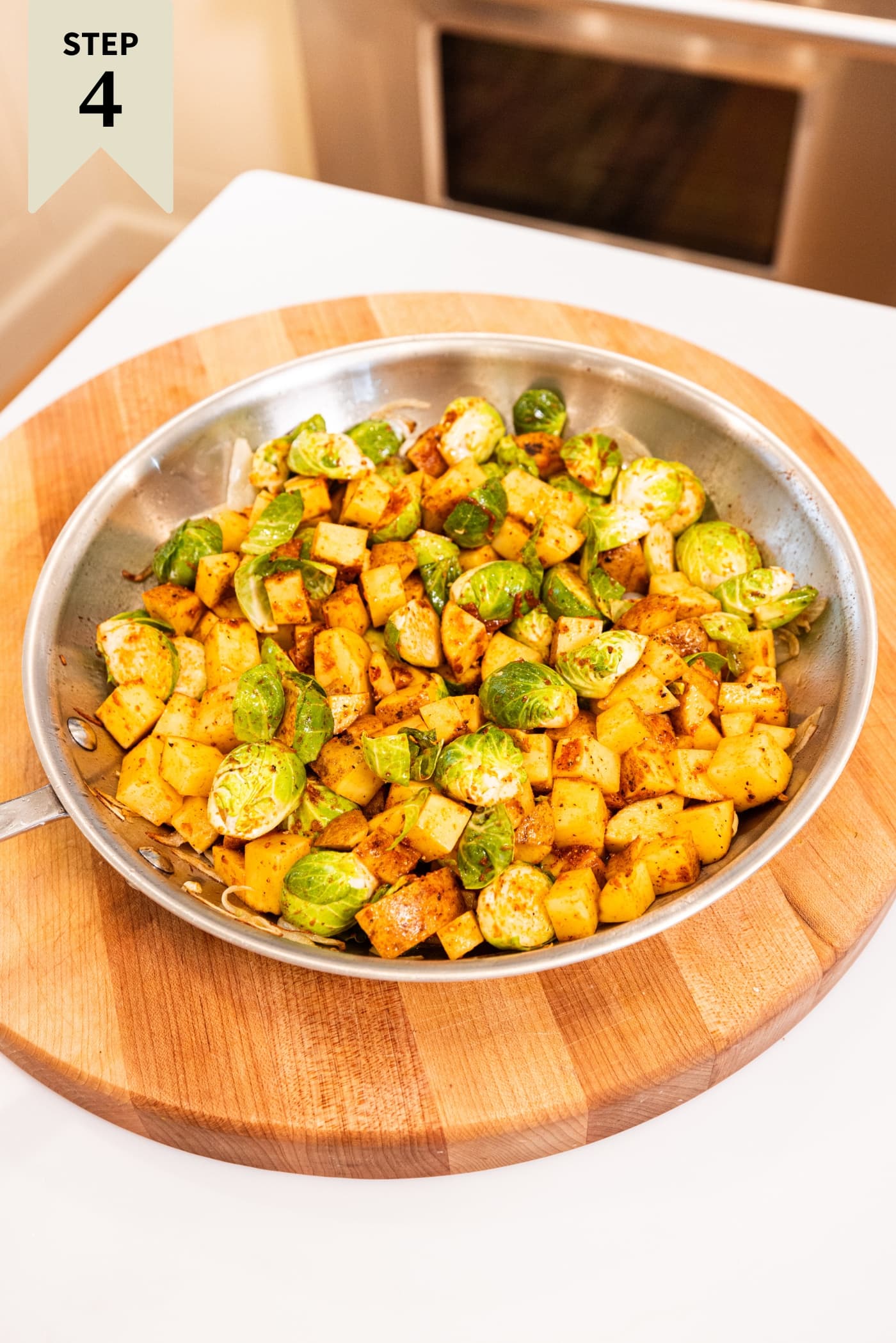 Metal skillet on wooden cutting board with sliced and spiced Brussels sprouts and potatoes before adding meat.