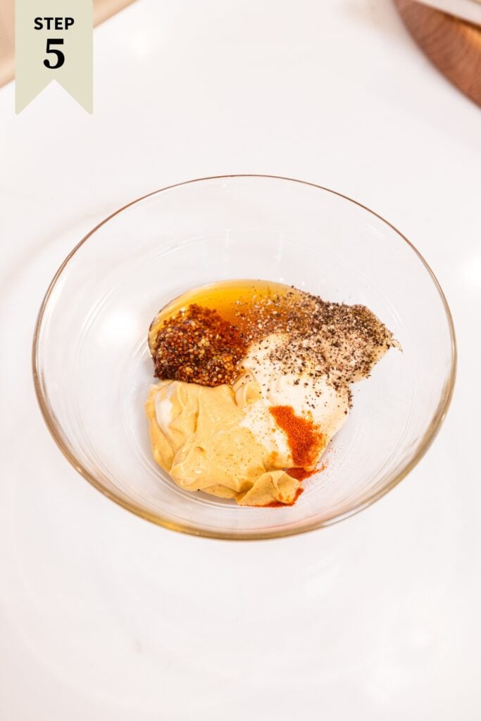 Glass bowl filled with a combination of ingredients needed for a homemade mustard sauce.