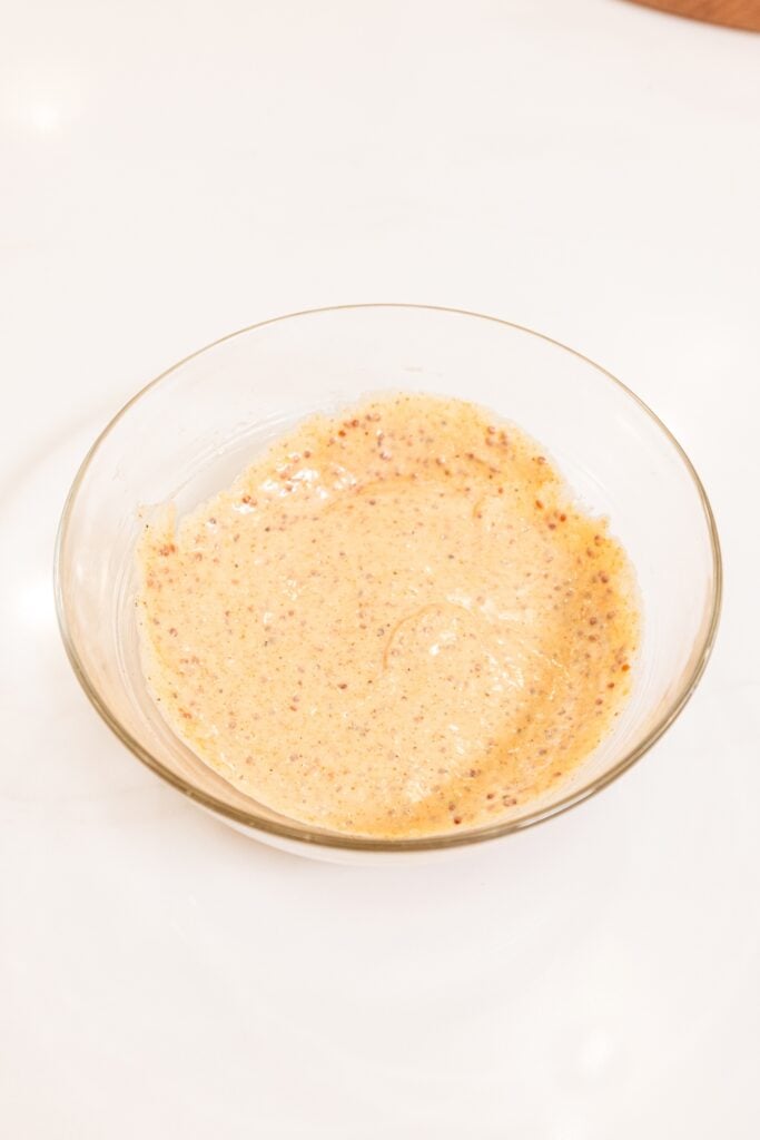 Glass bowl filled with homemade mustard sauce with whole-grain mustard seeds showing.