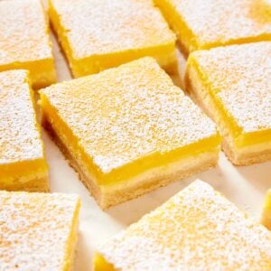 Lemon cheesecake bars resting on a white parchment surface dusted with powdered sugar showing each layer of the bar.