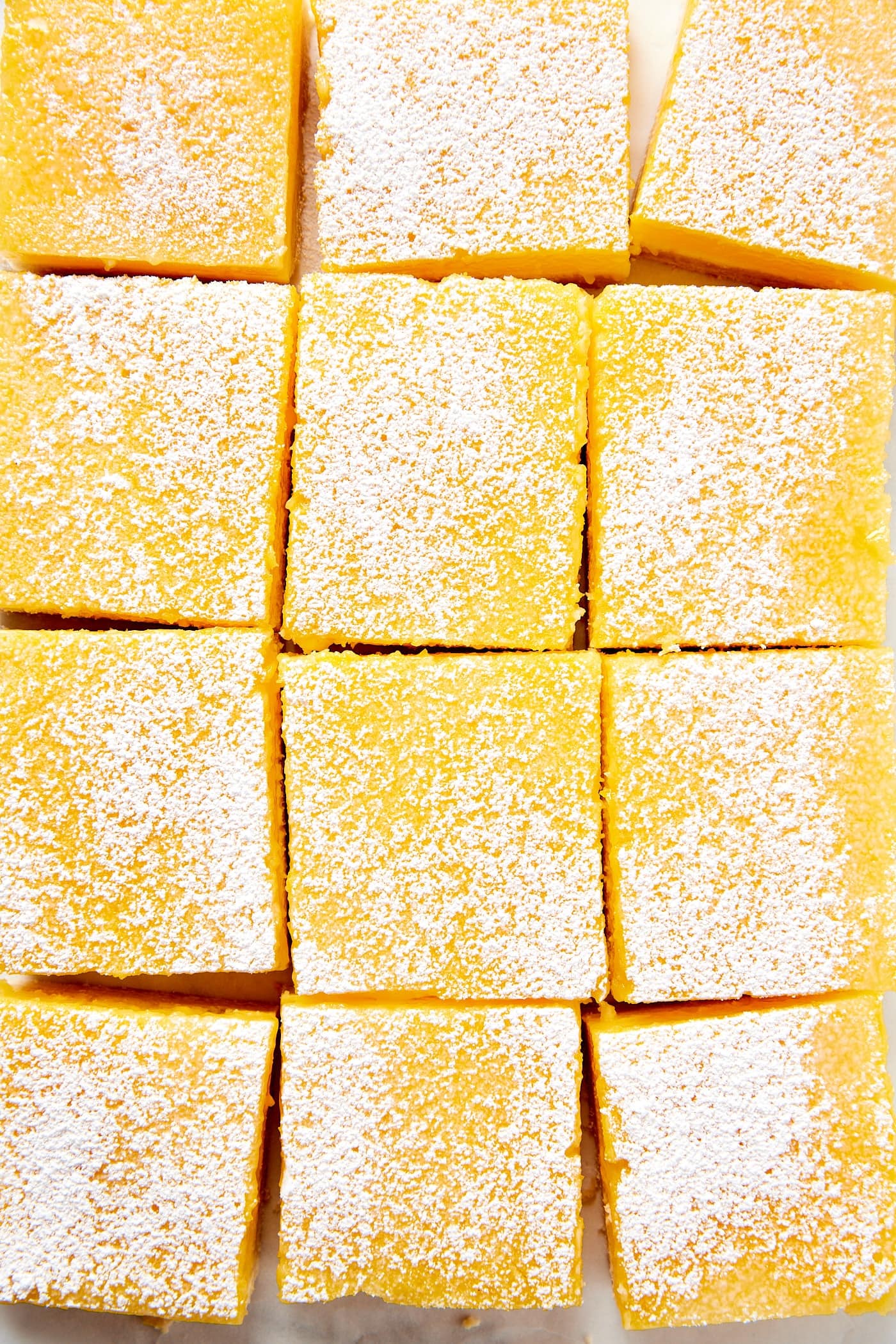 Squares of lemon cheesecake bars sitting on a piece of parchment lightly dusted with powdered sugar.