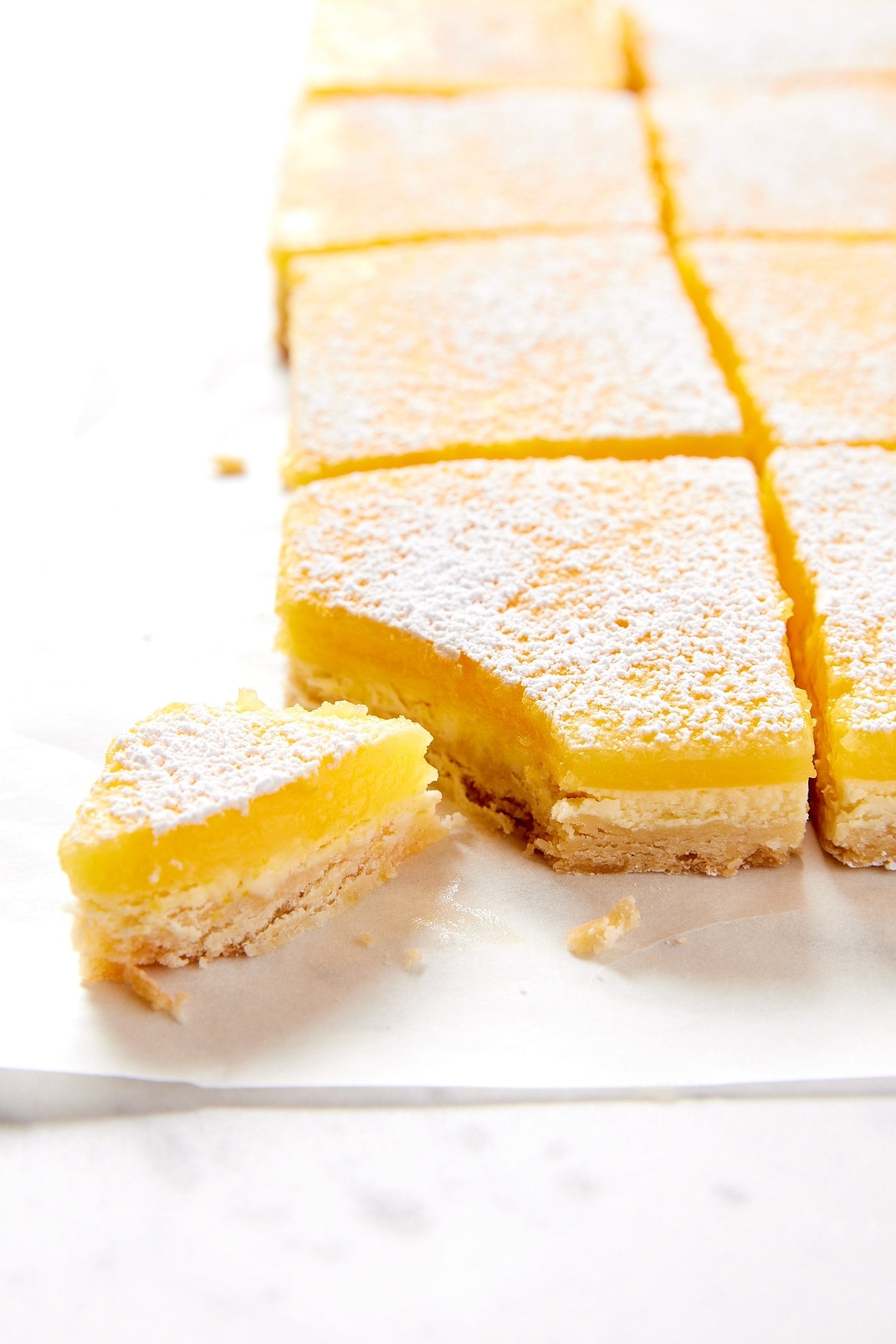 Squares of lemon cheesecake bars sitting on marble surface showing three interior layers including lemon and cheesecake and shortbread crust.
