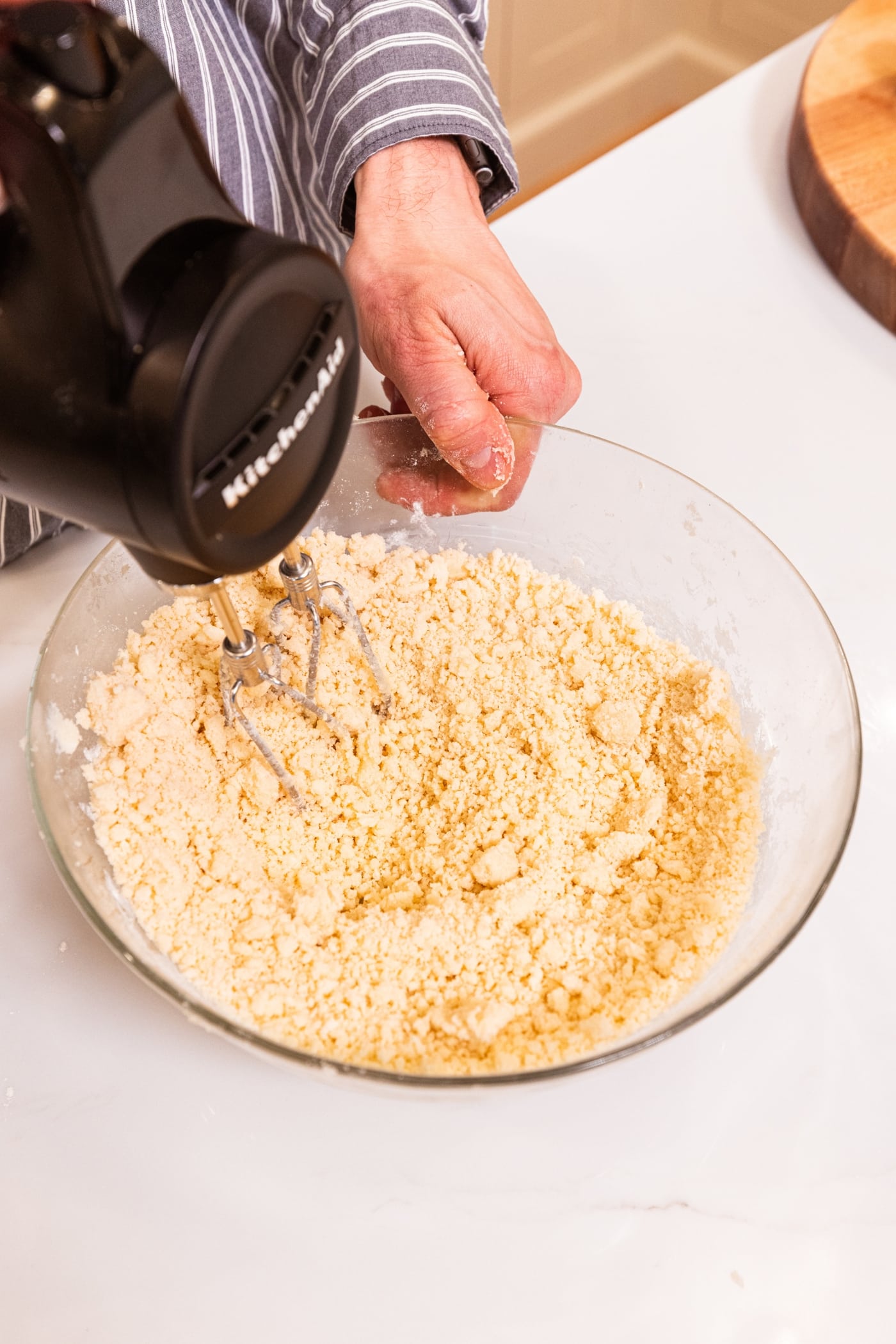 Handheld mixer mixing together shortbread mixture for a crust in a glass bowl.