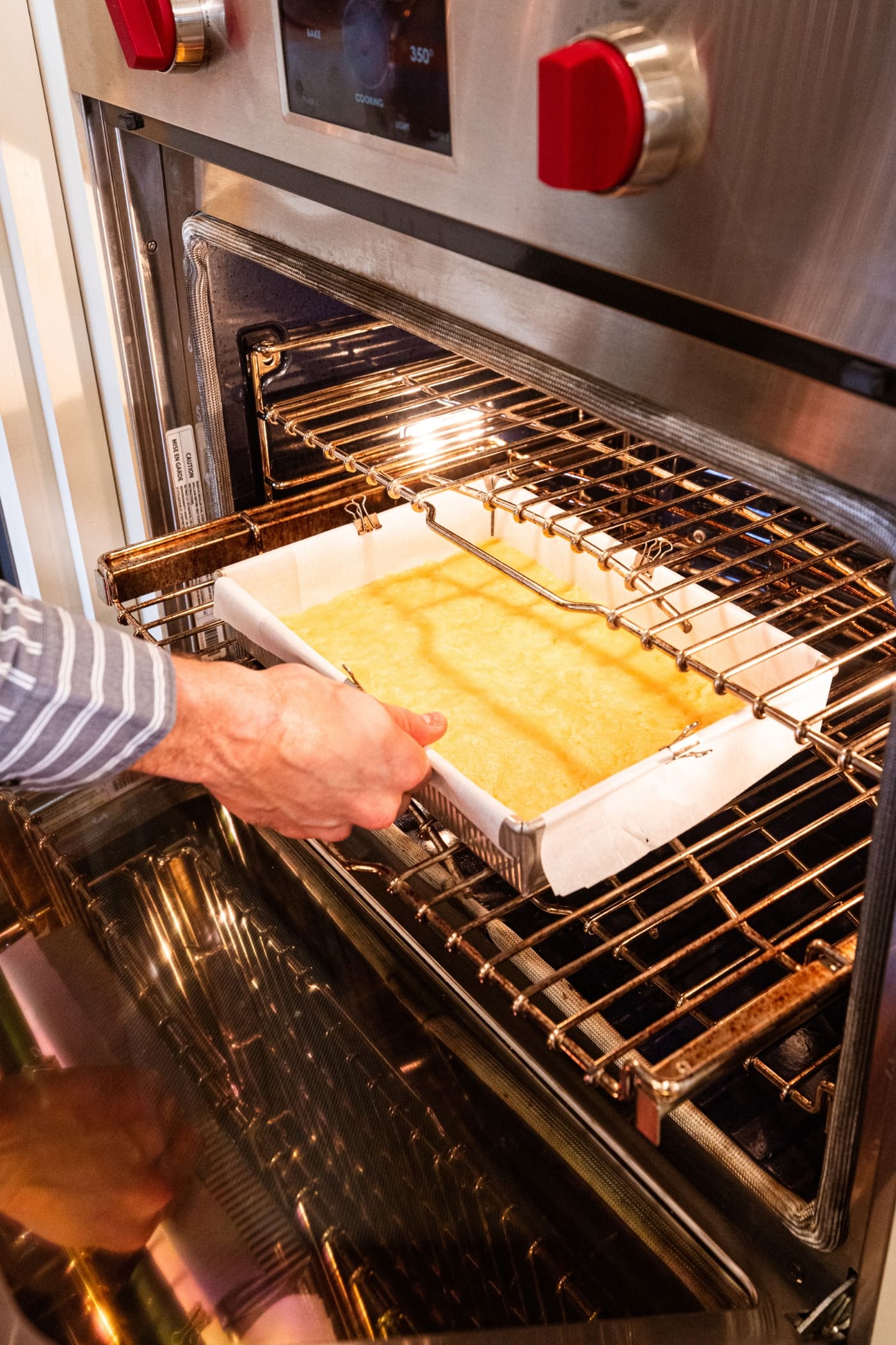 Hand placing 9x13 baking dish into a hot oven with a shortbread crust in the pan to bake.