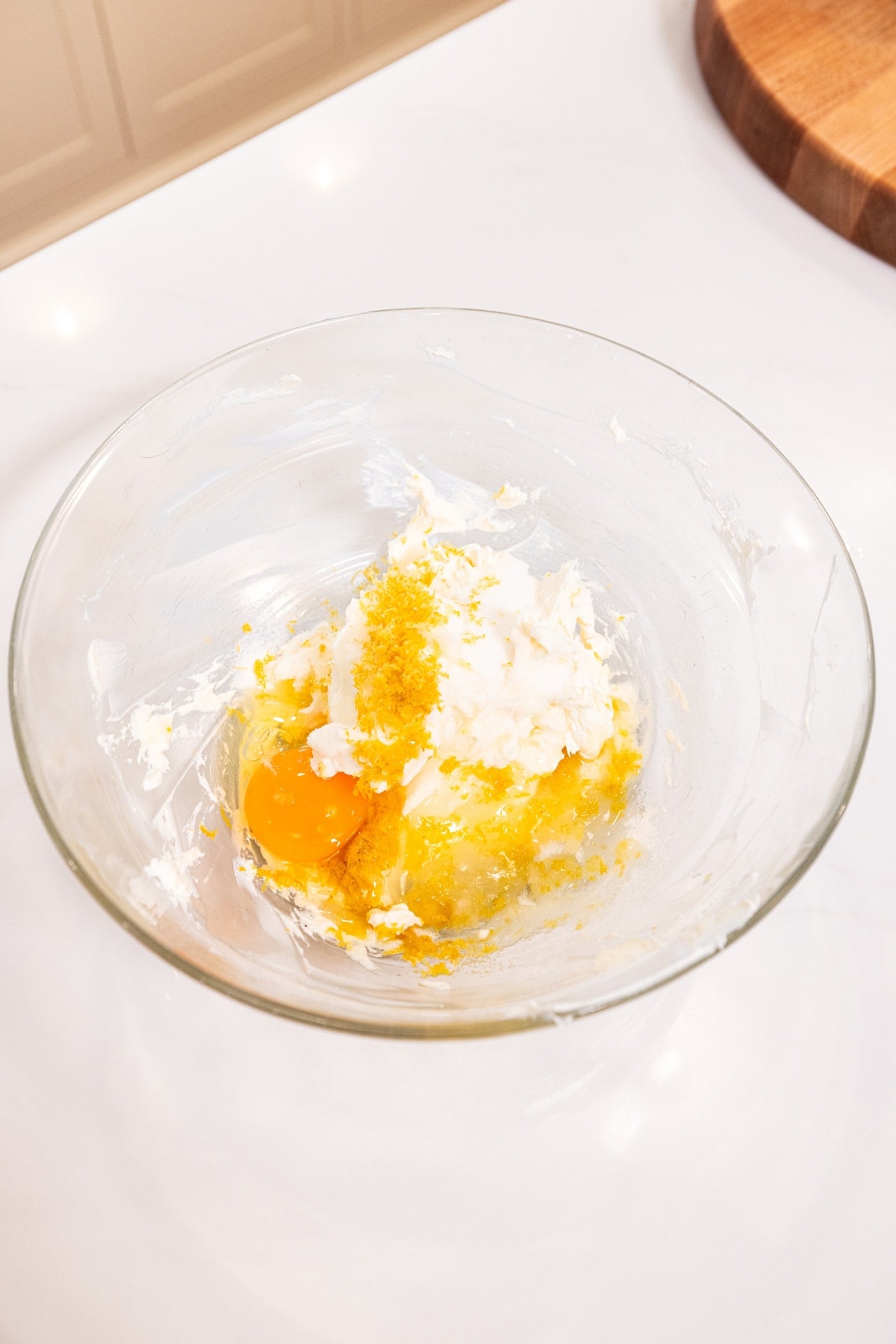 Large glass bowl filled with all wet ingredients needed for a cream cheese cheesecake filling for lemon bars.