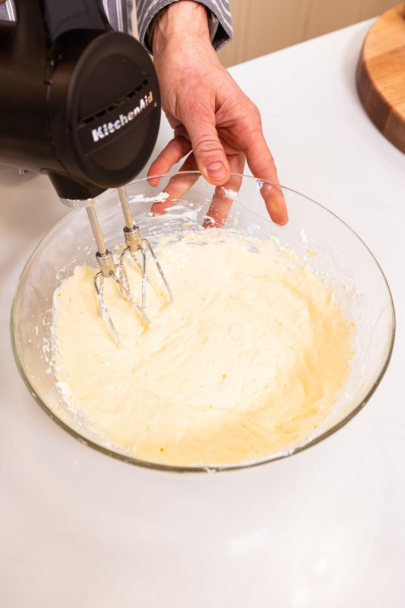 Glass bowl filled with liquid cheesecake layer to pour on top of crust layer being mixed with a handheld mixer.