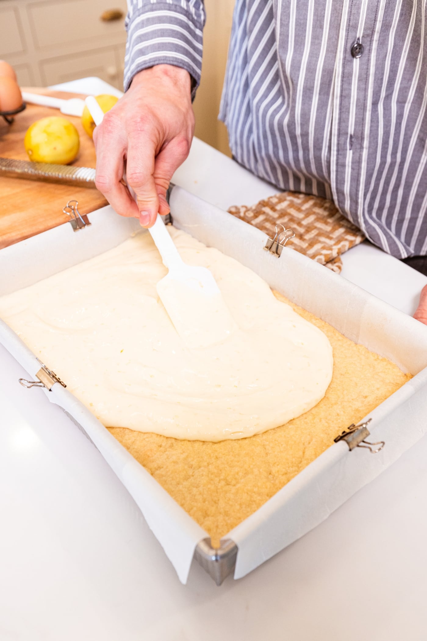 Rectangular baking dish with hand smoothing out liquid cheesecake mixture over the top of shortbread crust.