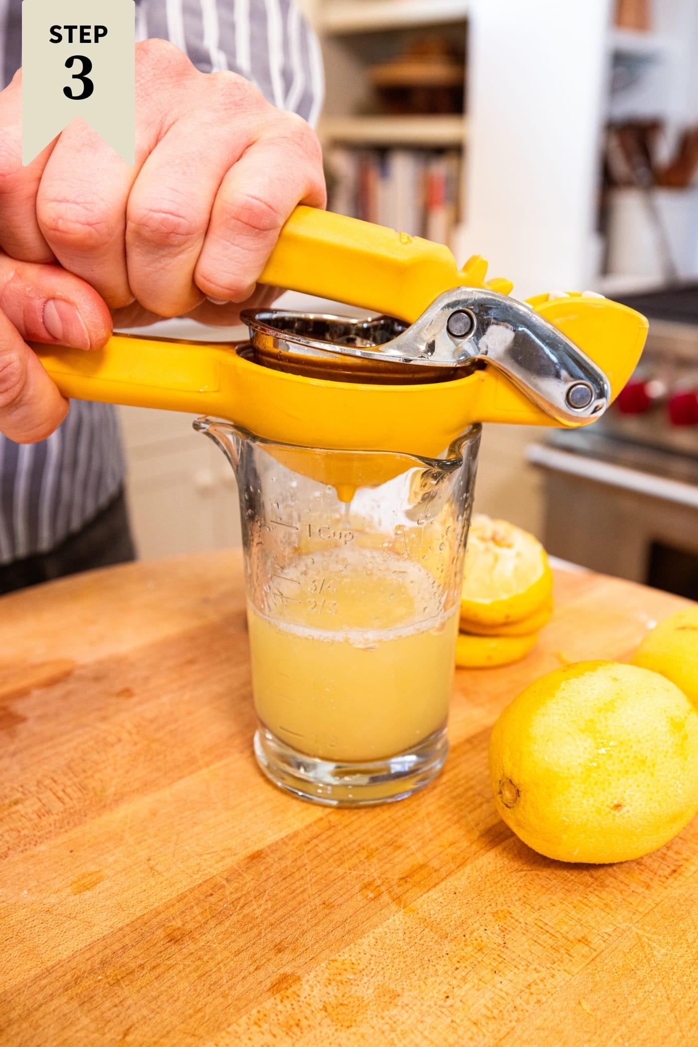 Hand squeezing lemon juice into a glass container on a wooden cutting board.