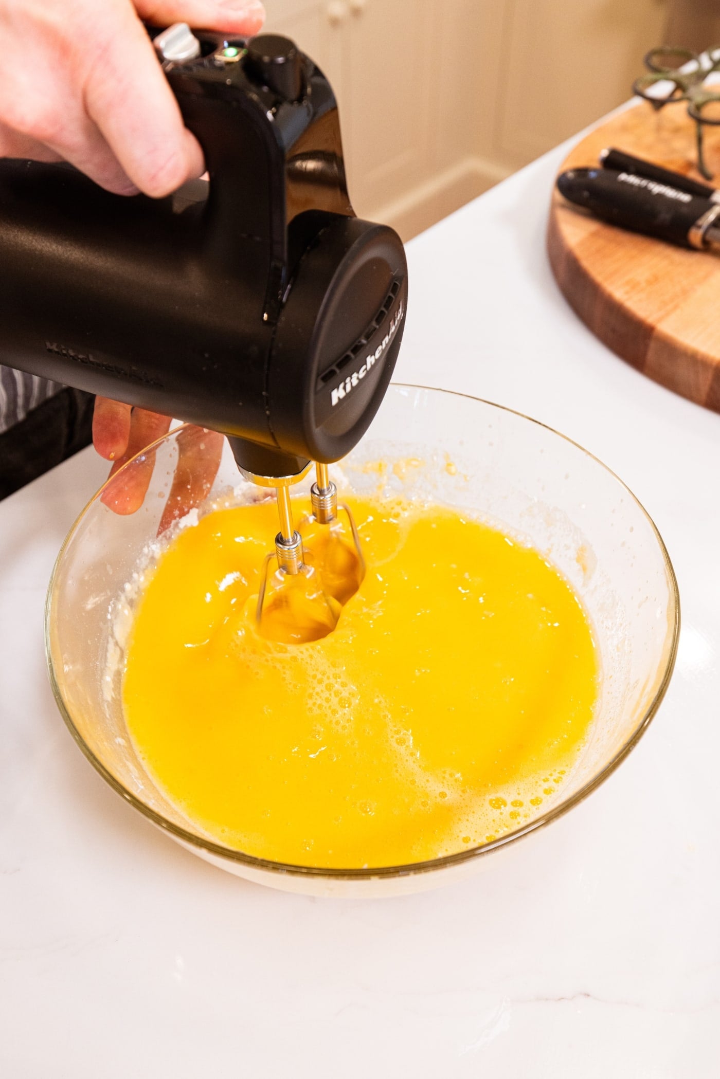 Handheld mixer mixing together lemon bar filling to pour on top of lemon cheesecake bars before being baked.