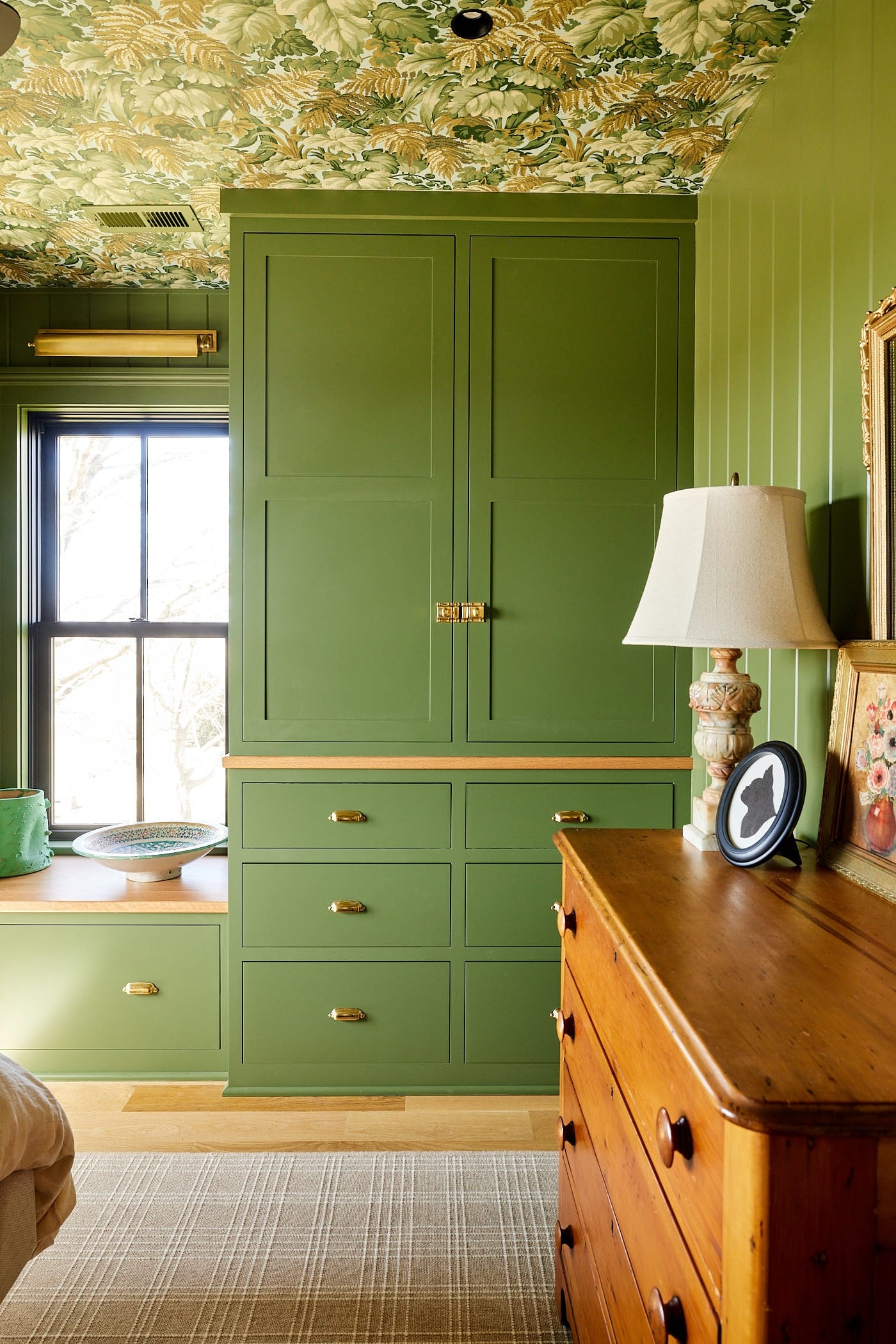 Built-in cabinets in bright green color with brass hardware with window seat to the side with pine hutch to the front.