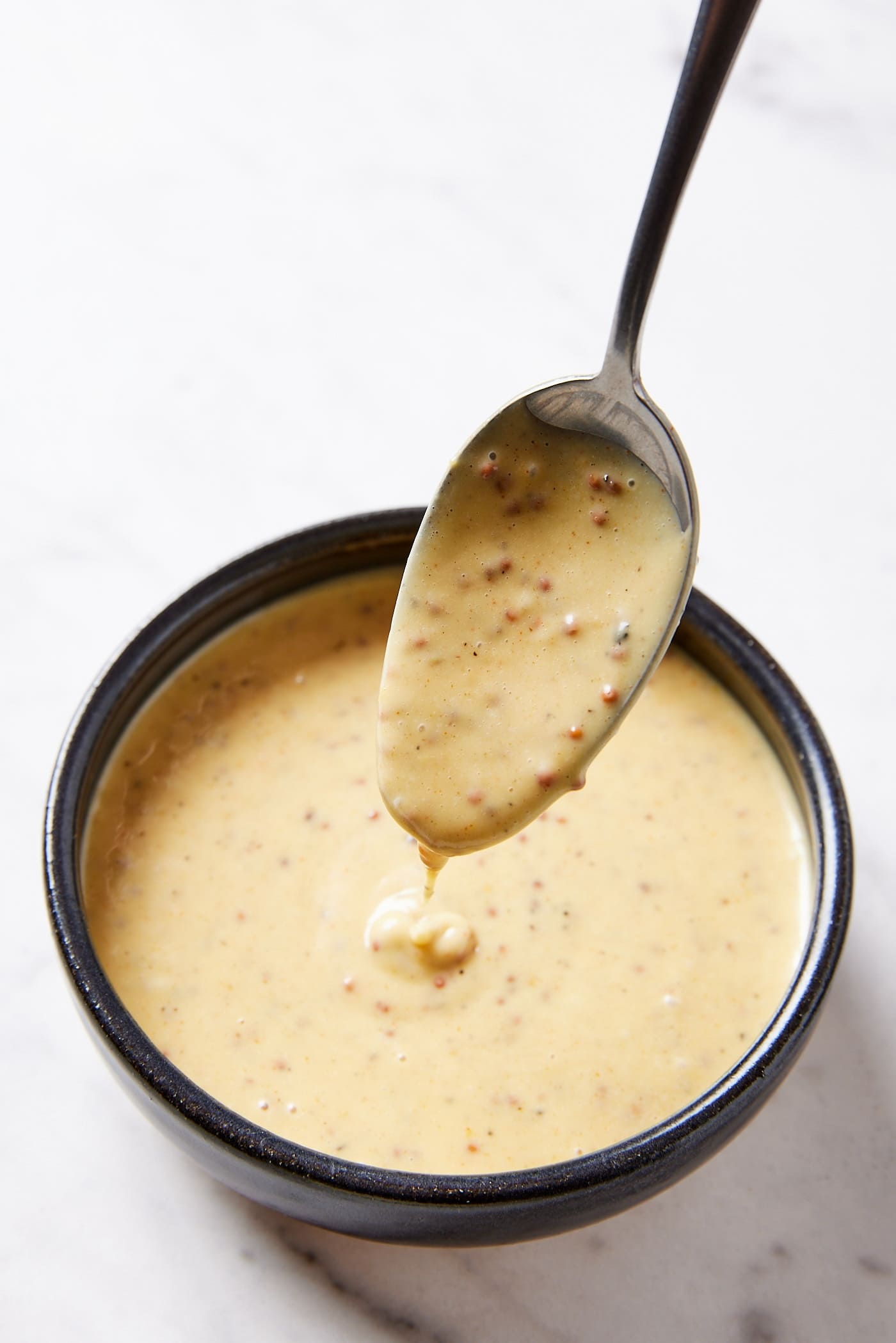 Small black bowl filled with mustard sauce with spoon drizzling some back into the bowl.