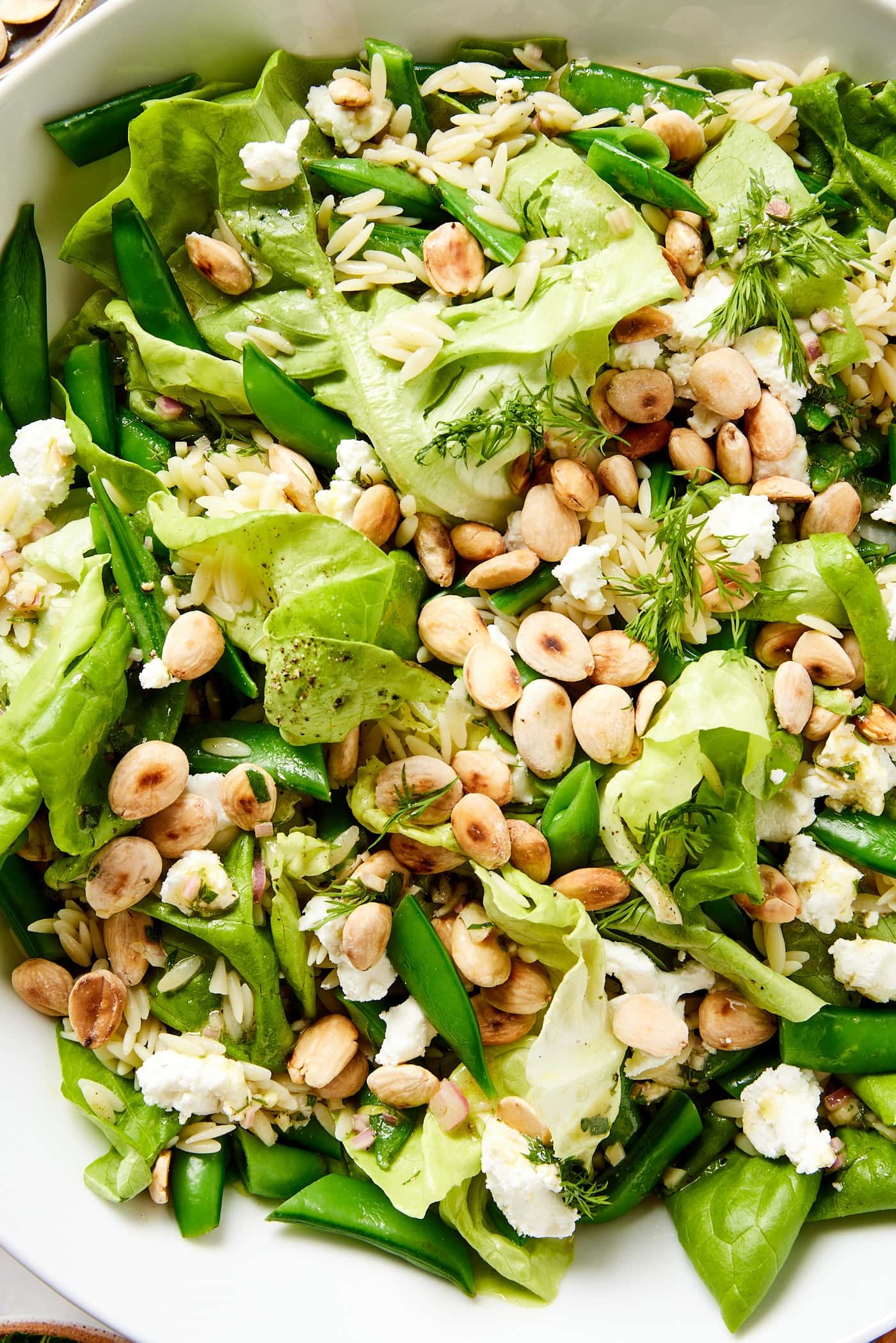 Salad bowl with spring orzo salad with Marcona almonds and snap peas sprinkled on top.