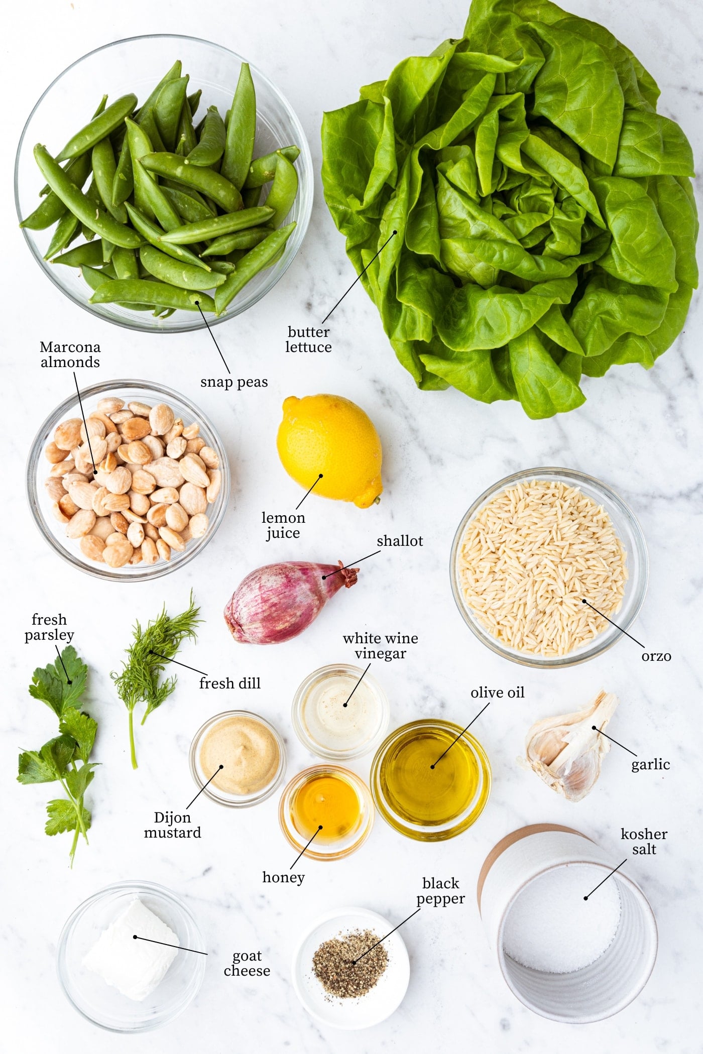 White marble surface filled with ingredients needed to make a spring orzo salad including lettuce, spices, snap peas, and orzo.