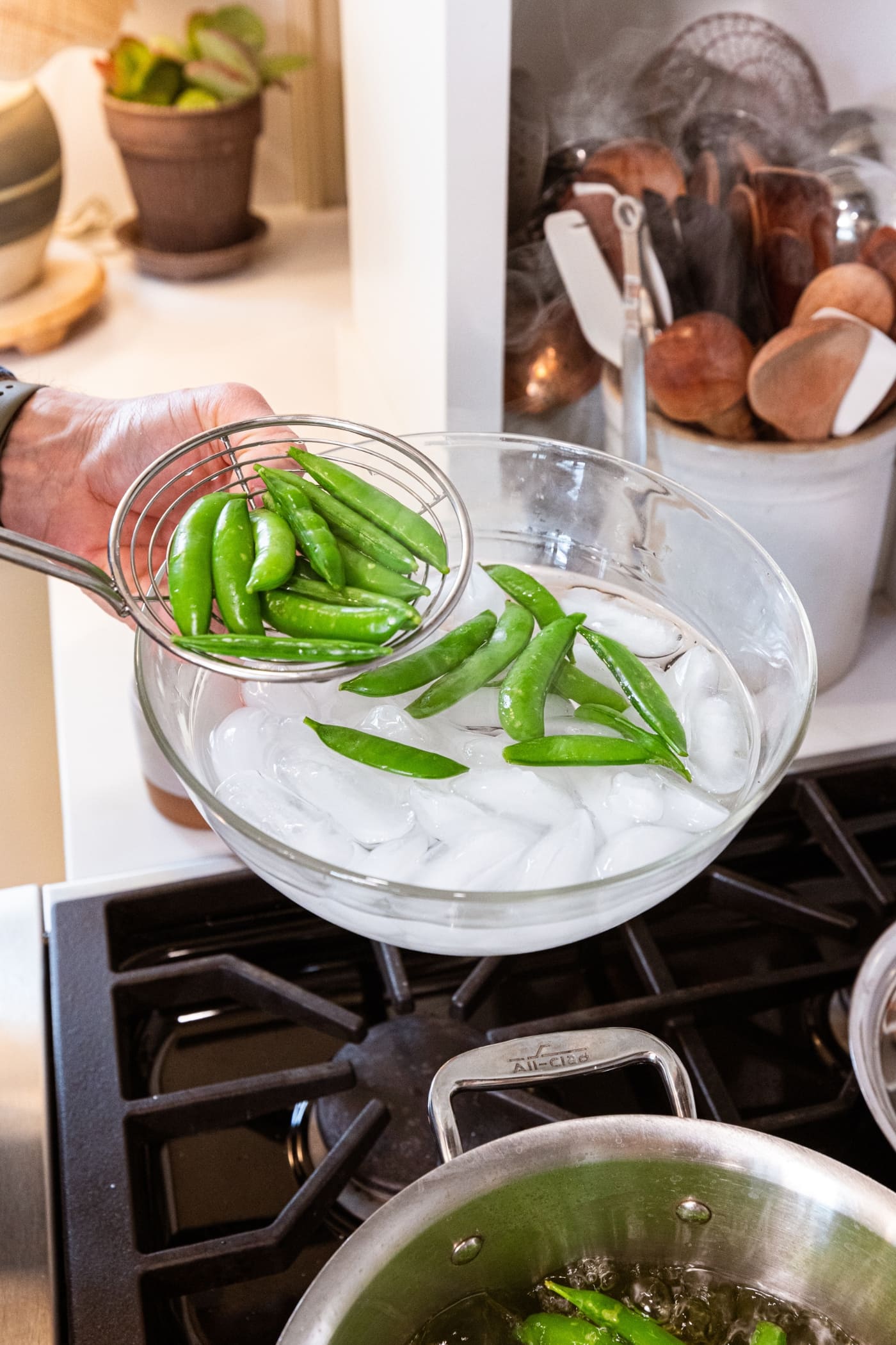 Glass bowl filled with ice water with snap peas being placed inside to chill.