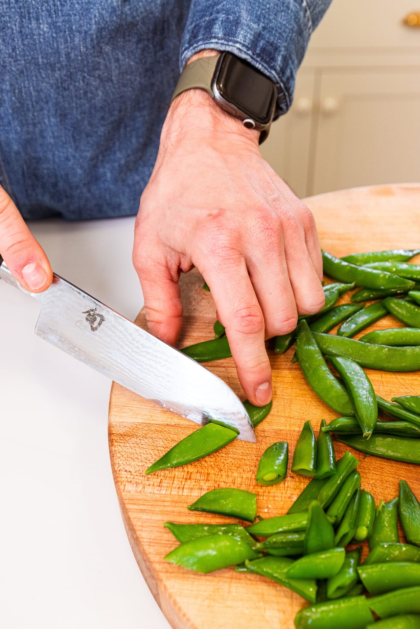 Hand using knife to slice snap peas in half before adding to a salad.