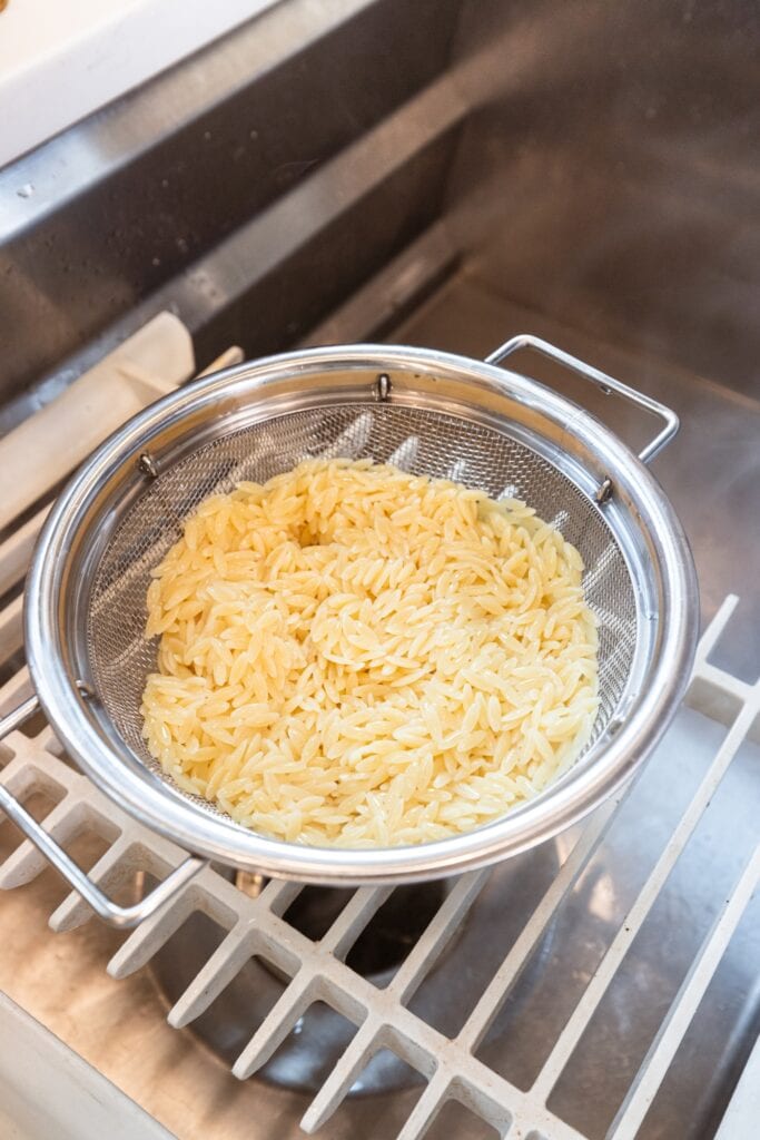 Colander sitting in a sink with draining orzo inside after being cooked on the stove.
