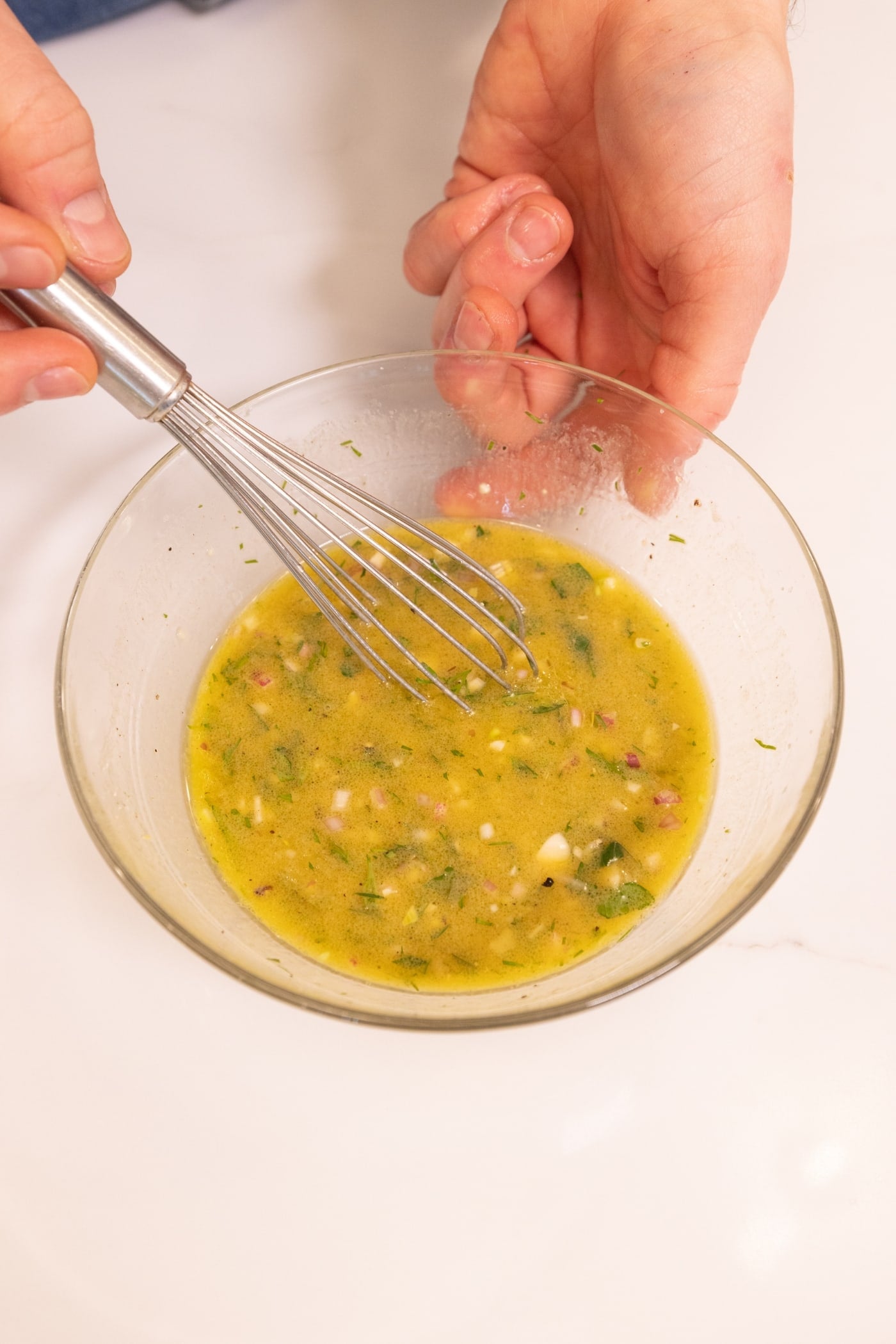 Hand mixing together a vinaigrette salad dressing for a spring salad in a small glass bowl.