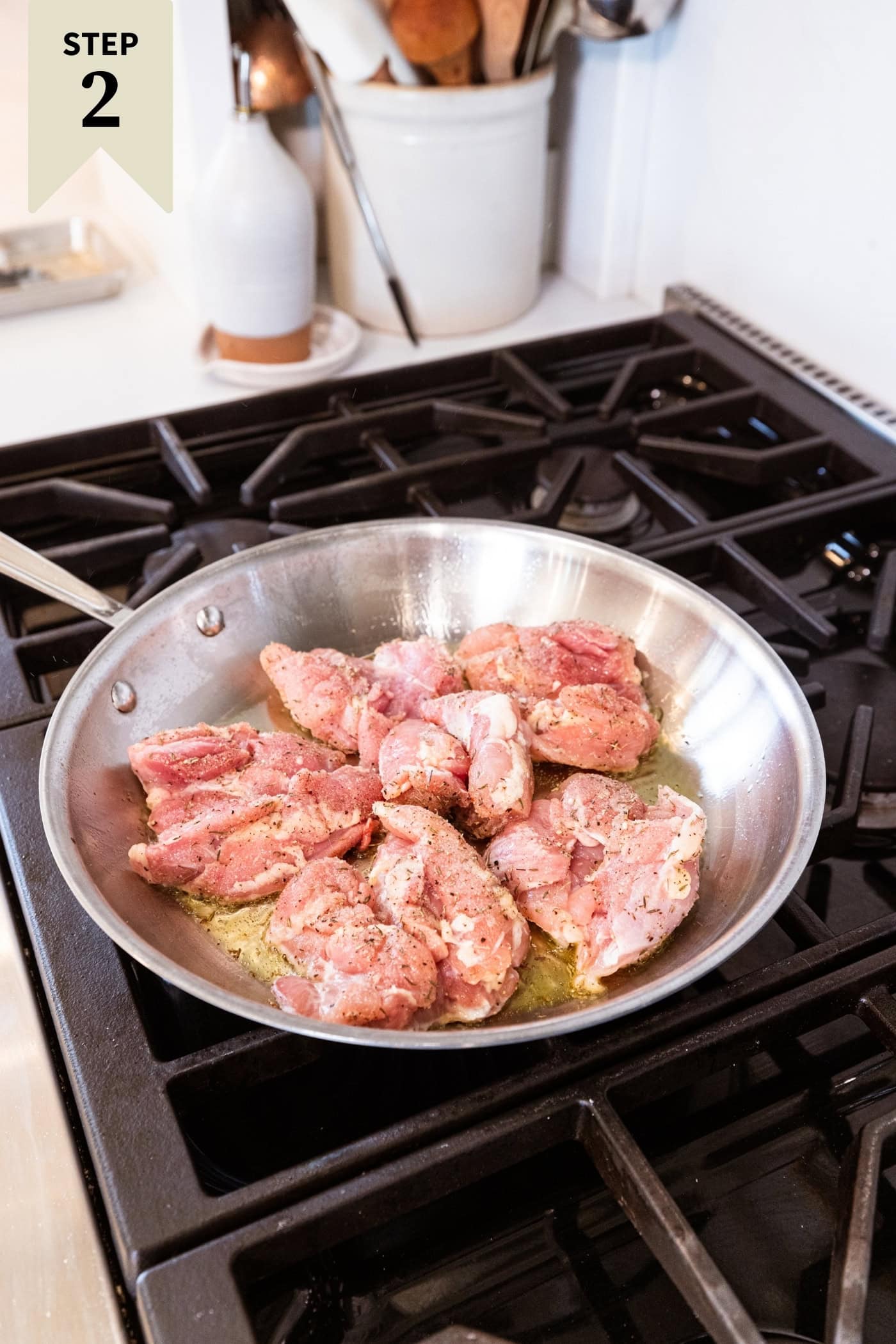 Raw marinated chicken thighs in a metal skillet on the stovetop browning on one side.