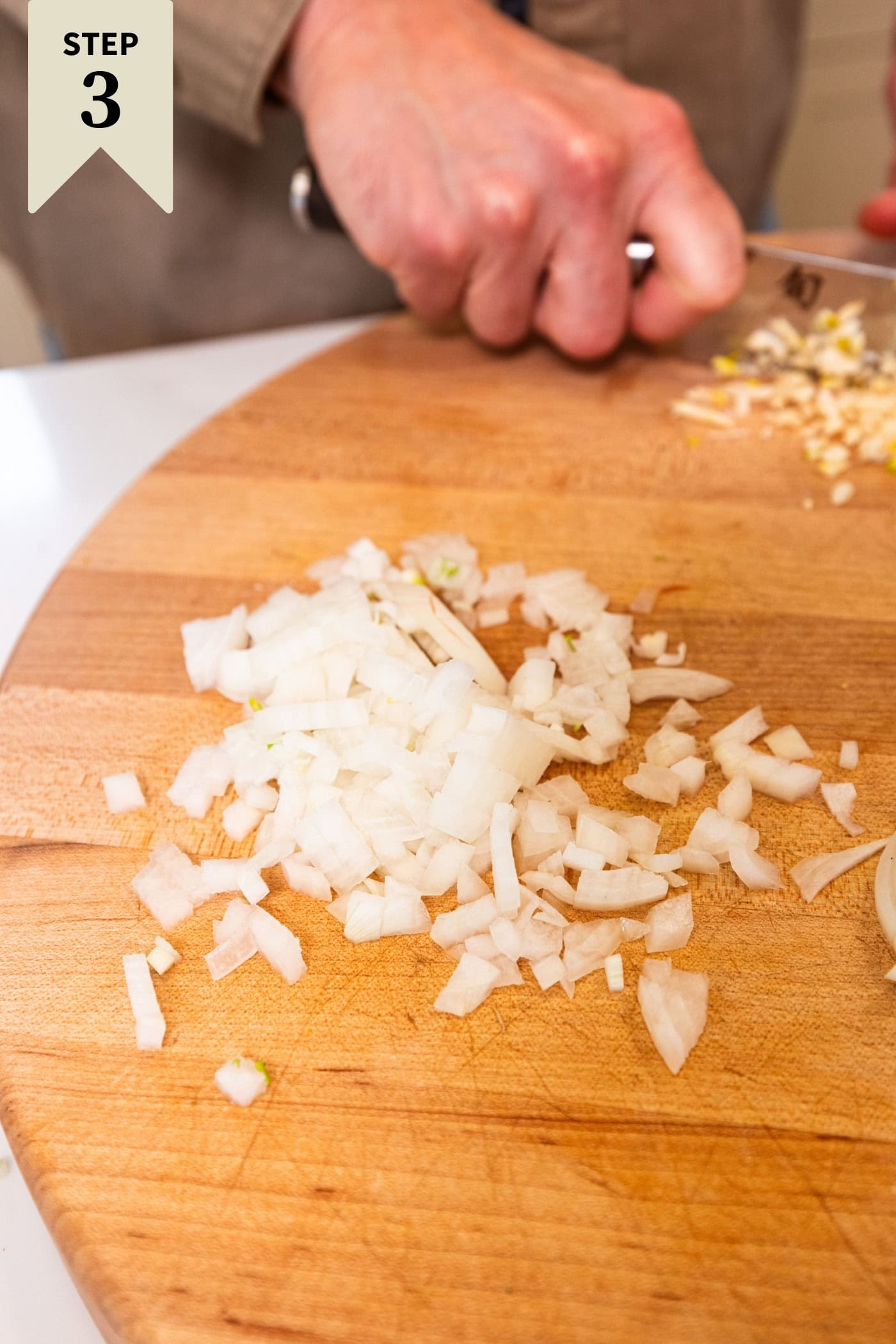 Chopped onion sitting on a wooden cutting board before being cooked.