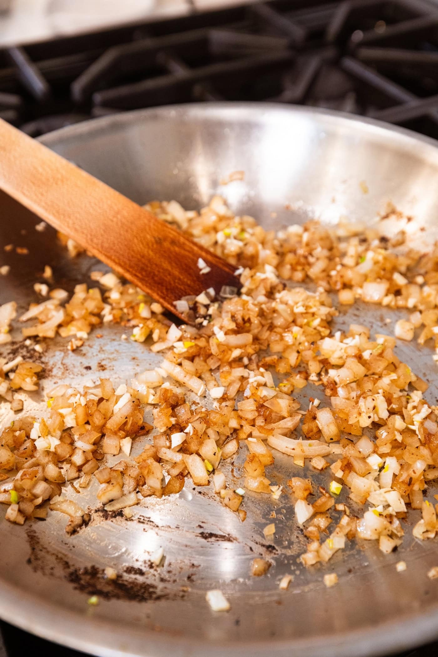 Browned diced pieces on onion in a metal skillet on the stovetop being stirred with a wooden spatula.