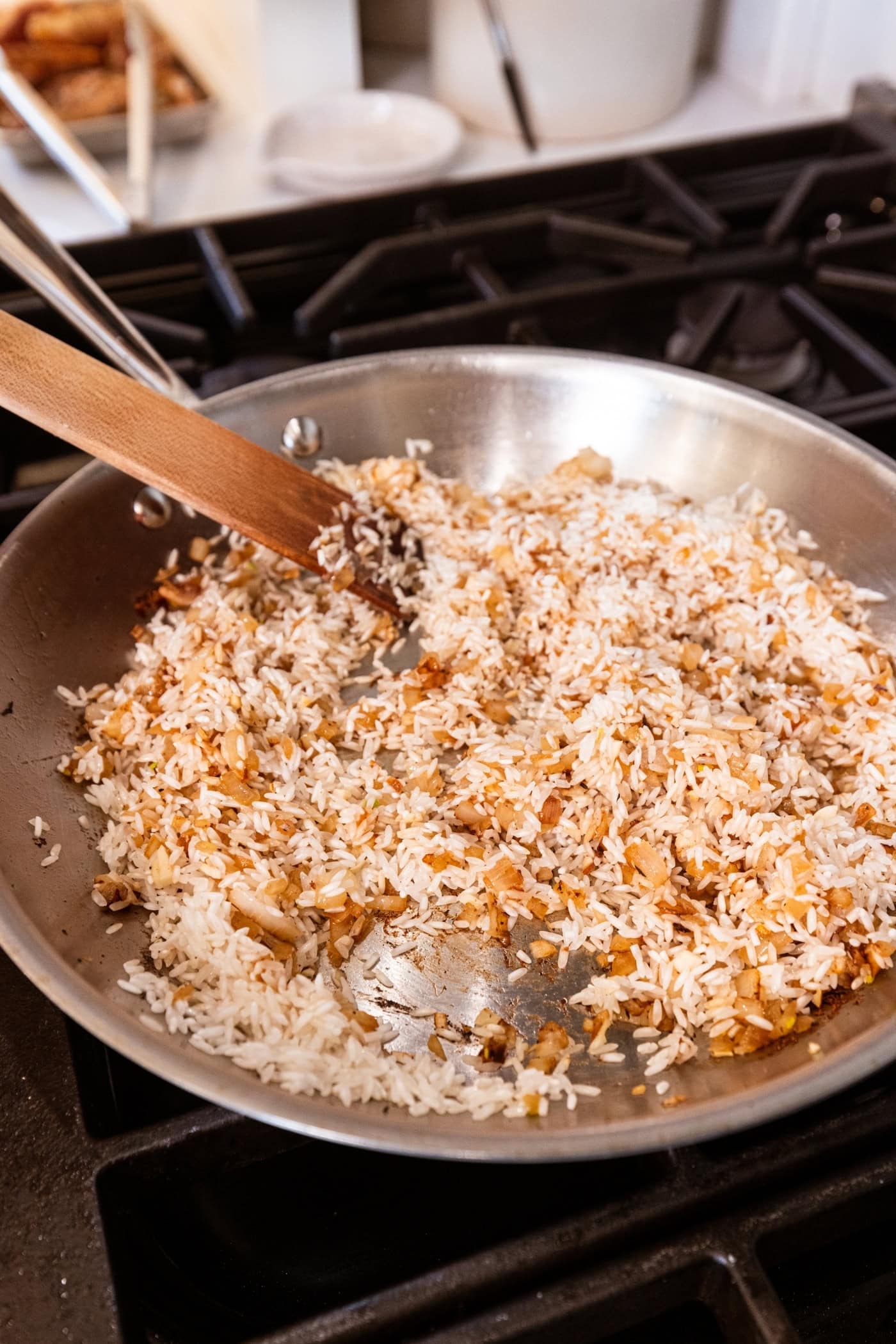 Rice mixed with browned diced onion being stirred together in a metal skillet.
