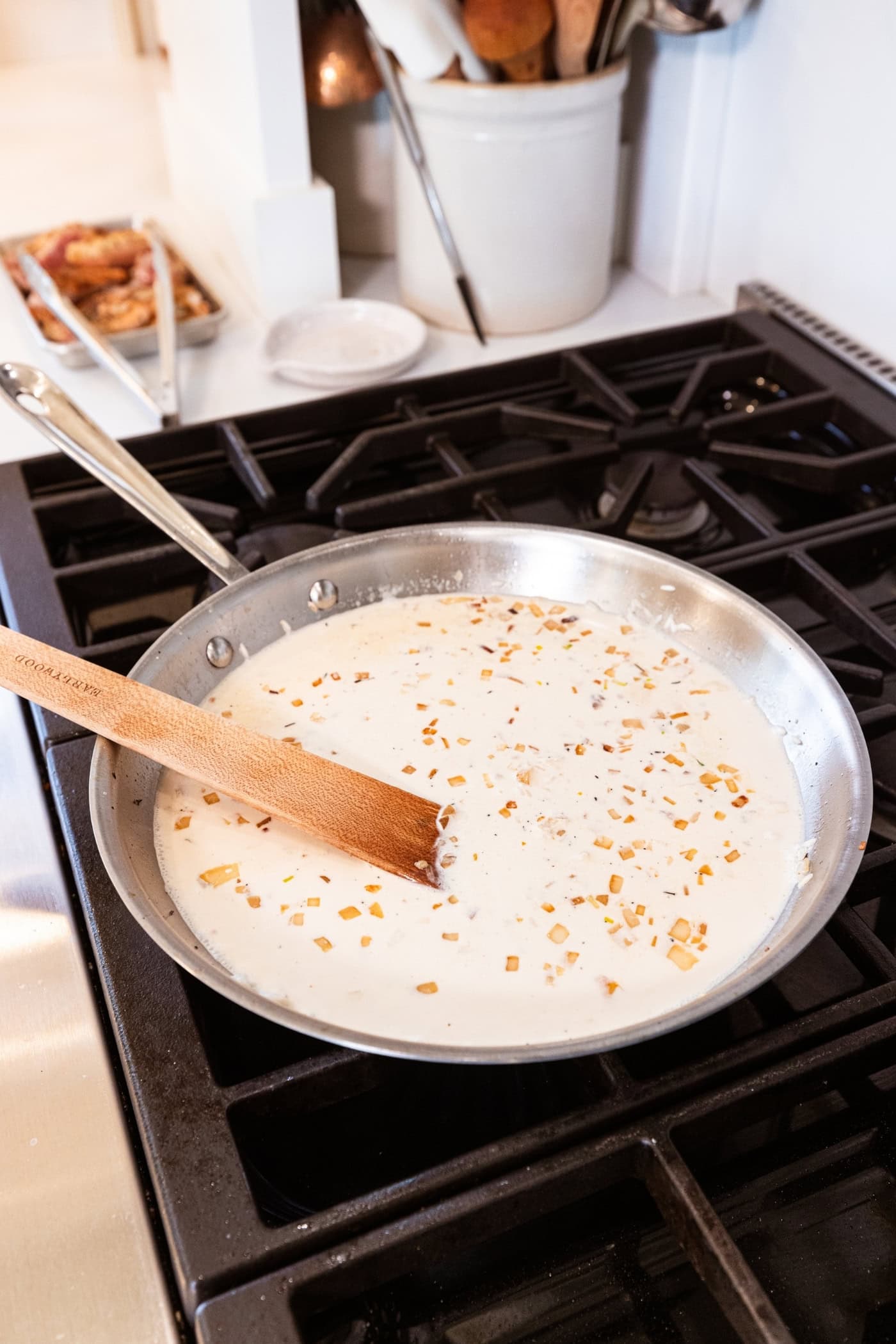 Metal skillet on a stovetop with cream and browned pieces of rice and onion being stirred together with a wooden spatula.