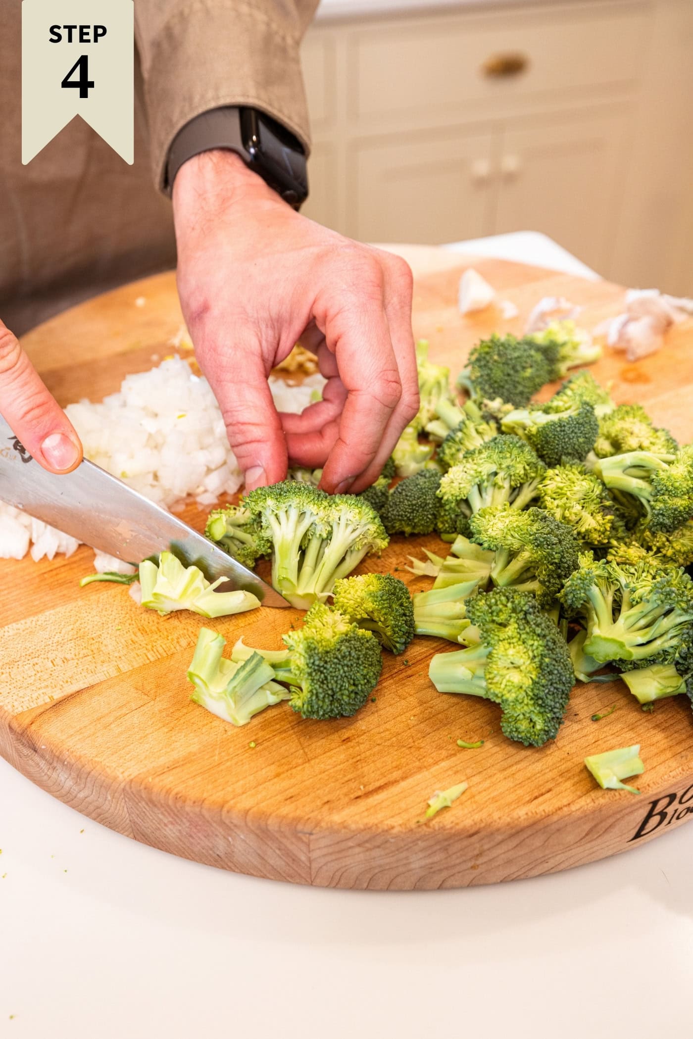 Hand using a knife to chop broccoli into smaller pieces on a wooden cutting board.