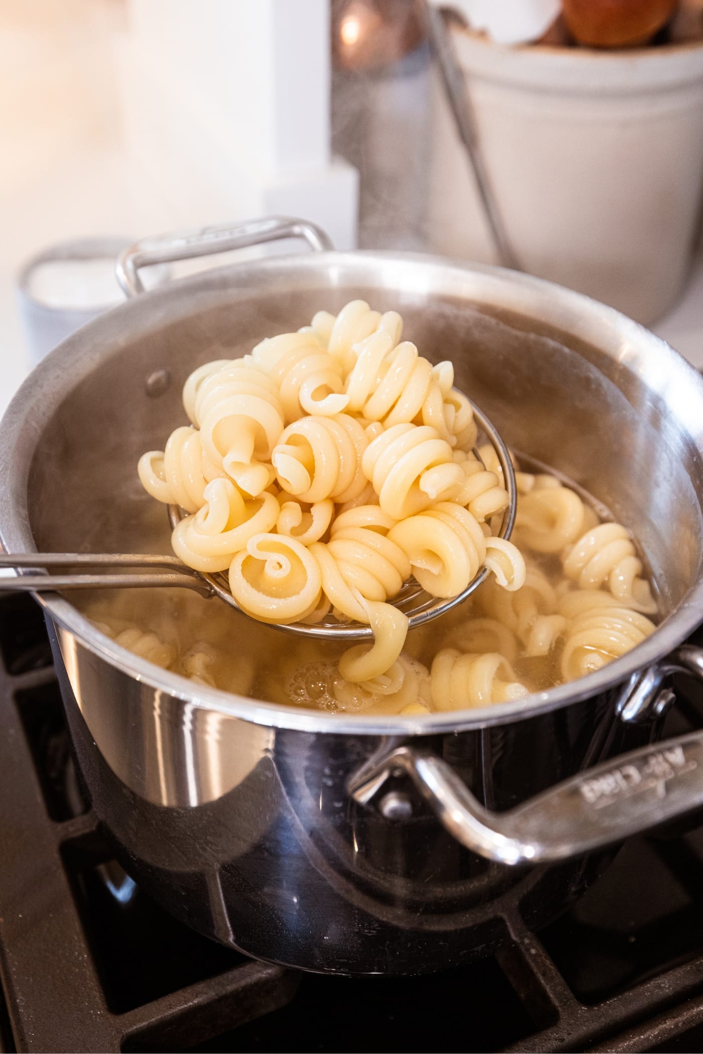 Hand using ladle to scoop up cooked twirled pasta from large stockpot on the stovetop.