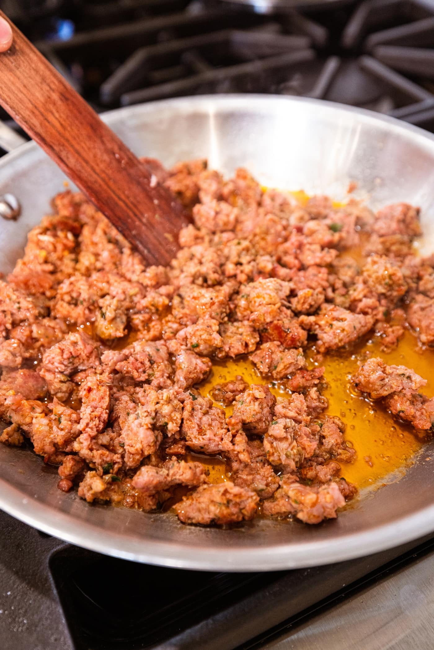 Cooking sausage in a metal skillet on the stovetop showing the oil coming out of the meat.