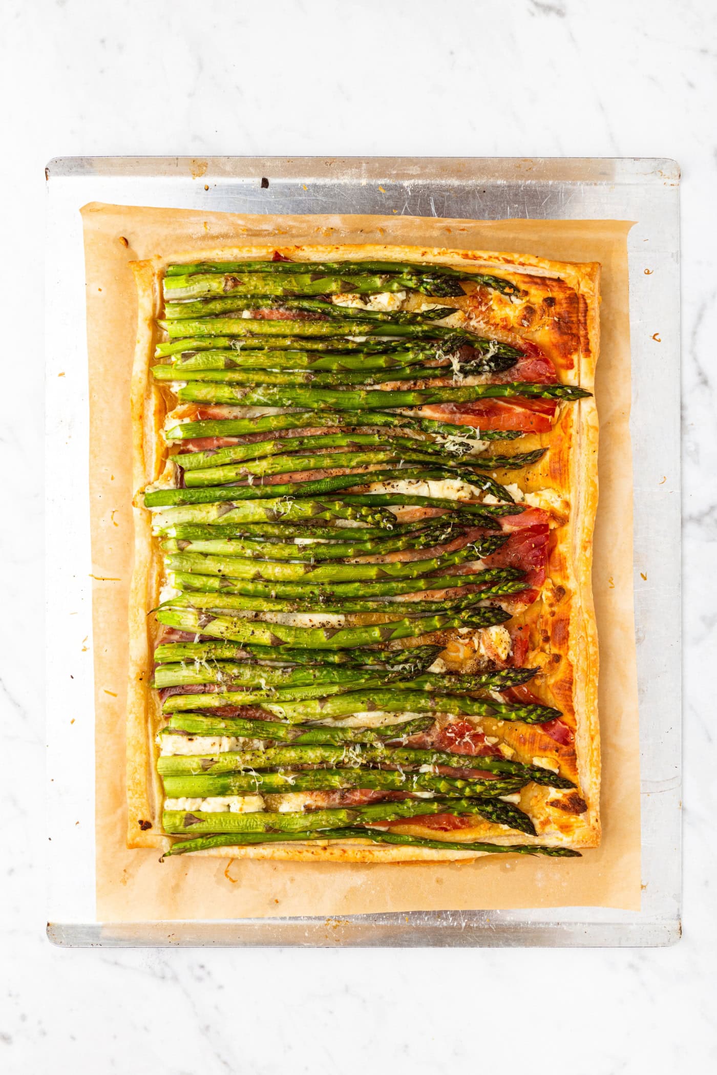 Baked asparagus tart made with asparagus stalks, Dijon mustard, and puff pastry on a baking sheet after coming out of the oven.