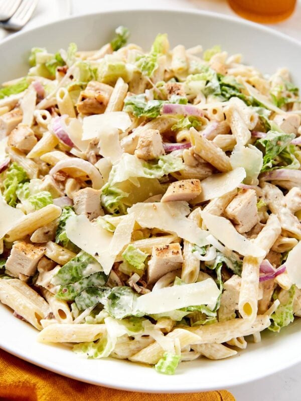 White bowl filled with chicken Caesar pasta salad with pieces of Parmesan cheese and red onion sprinkled on top.