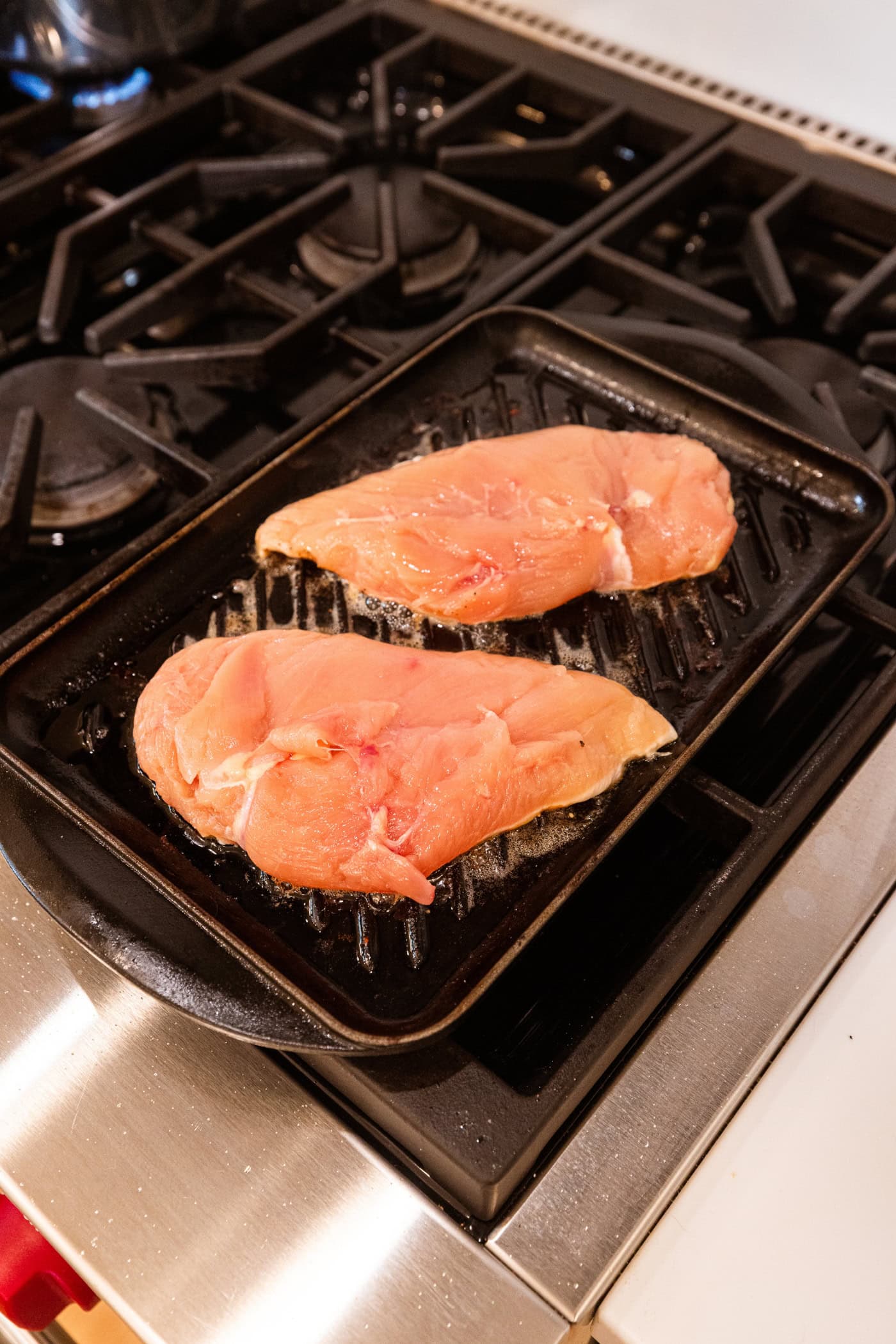 Raw chicken breasts on a grill pan being cooked on the stovetop.