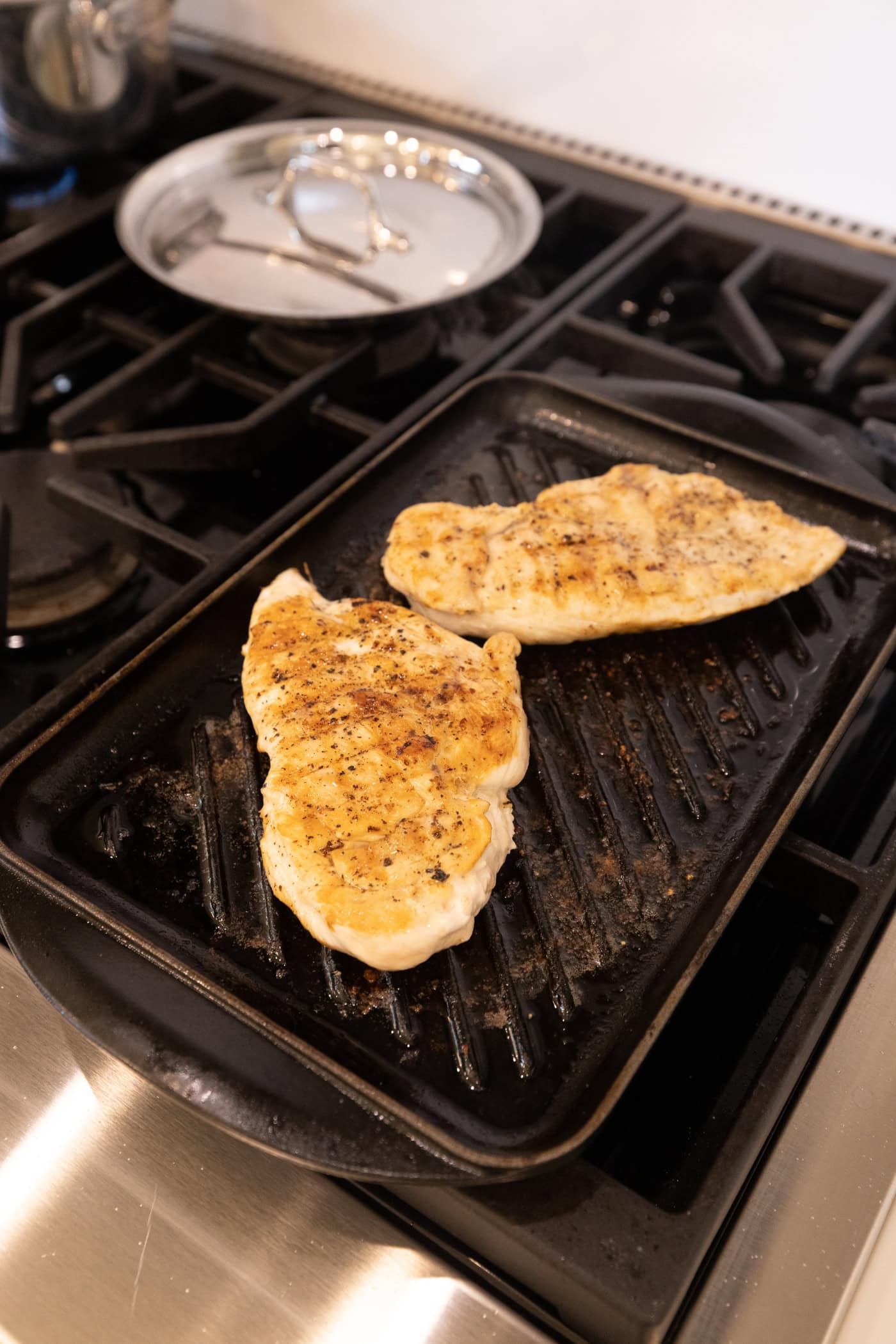 Two chicken breasts cooking on a grill pan on a stovetop with grill pattern on top.