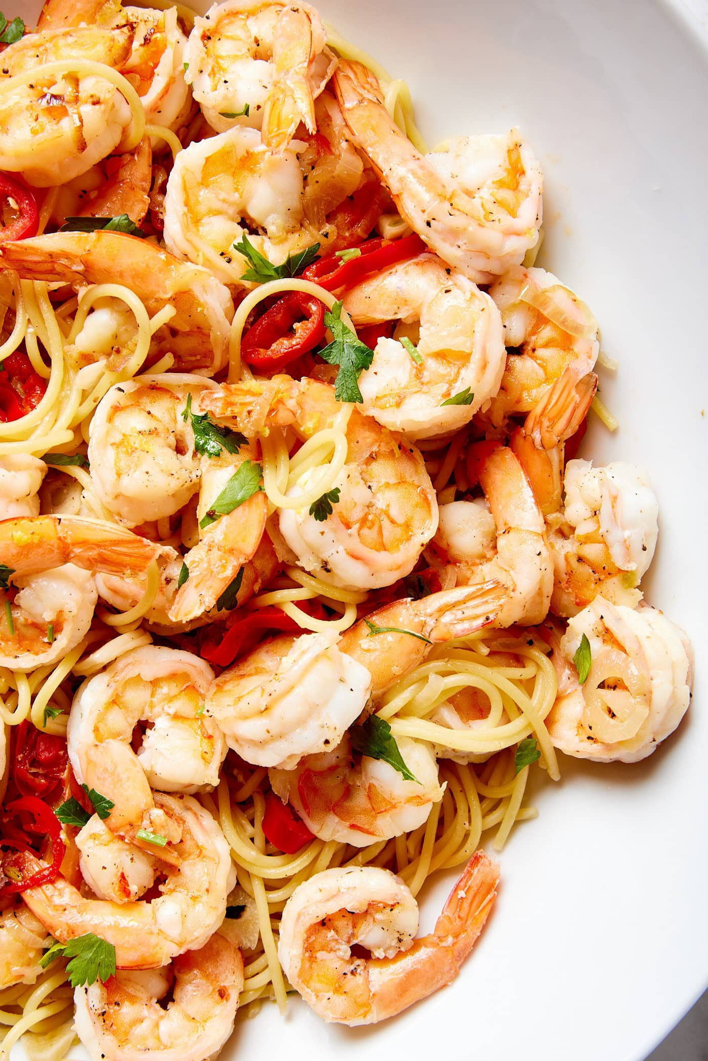 White bowl filled with garlic shrimp pasta with red chiles and spaghetti wrapping around the cooked pieces of shrimp.