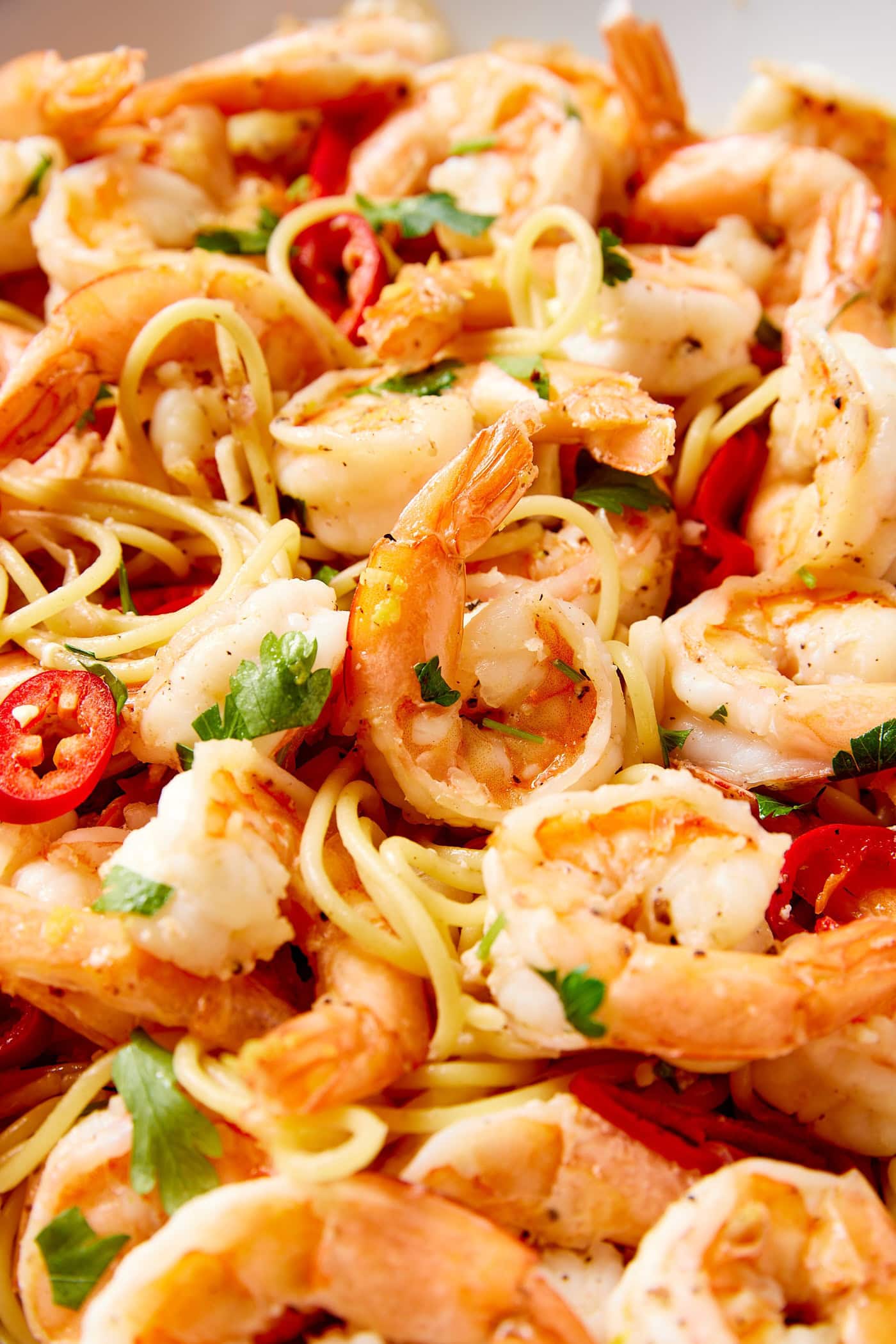 Large bowl filled with garlic shrimp pasta with spaghetti noodles wrapping around the pieces of shrimp with red chiles.