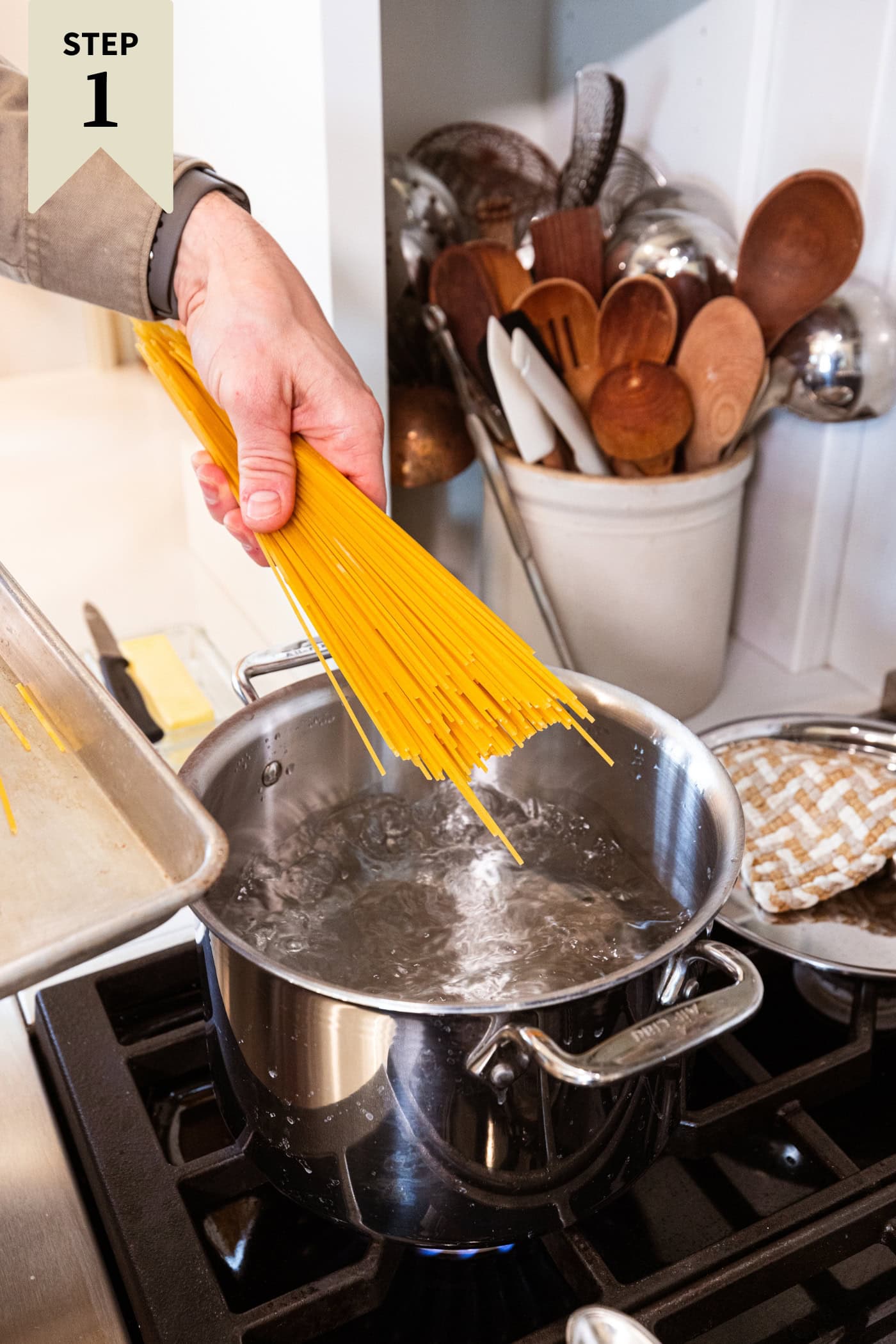 Raw spaghetti being placed in a large pot on the stovetop filled with boiling water.
