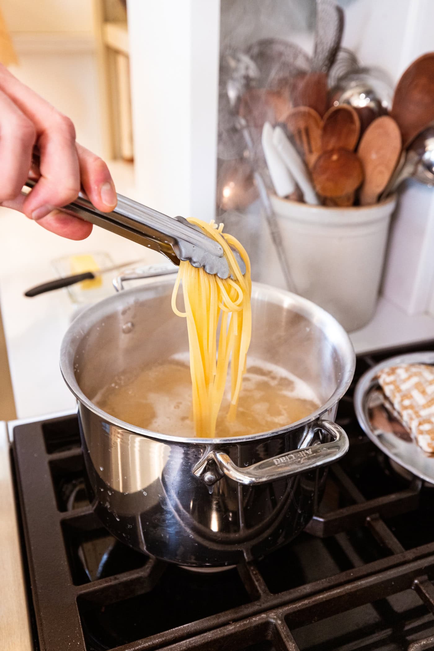 Hand using tongs to scoop out cooked spaghetti from a large stockpot on the stove.