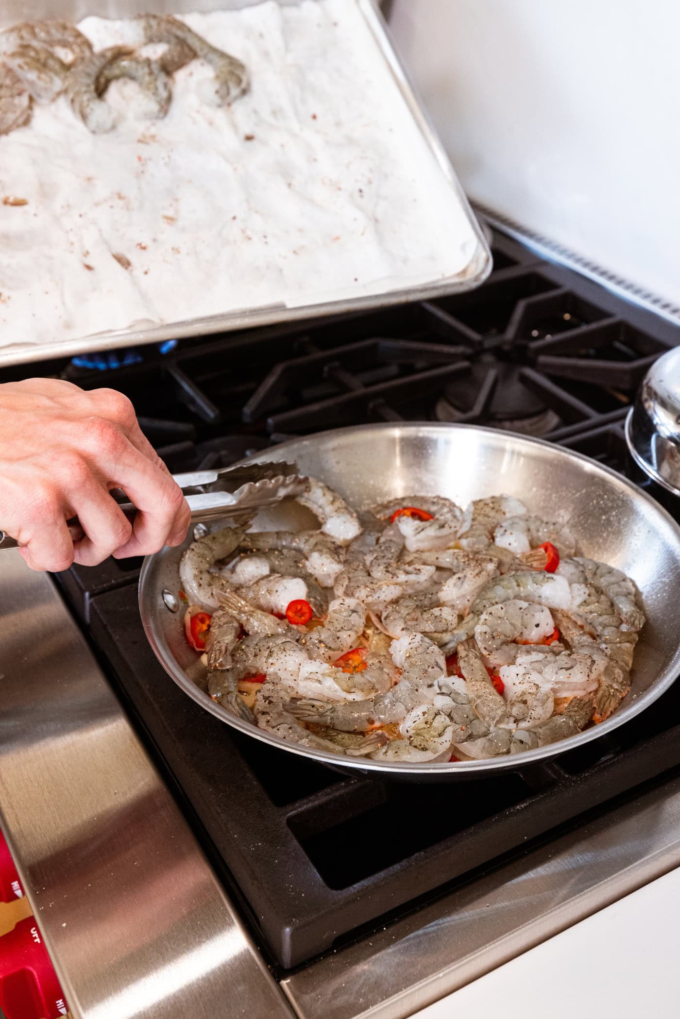 Hand placing raw shrimp in a large skillet with a tongs to cook for garlic shrimp pasta.