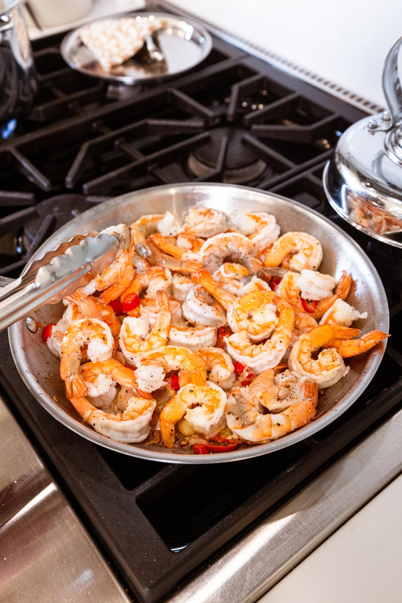Cooked, brightly colored shrimp with red chiles in a large skillet on the stovetop.