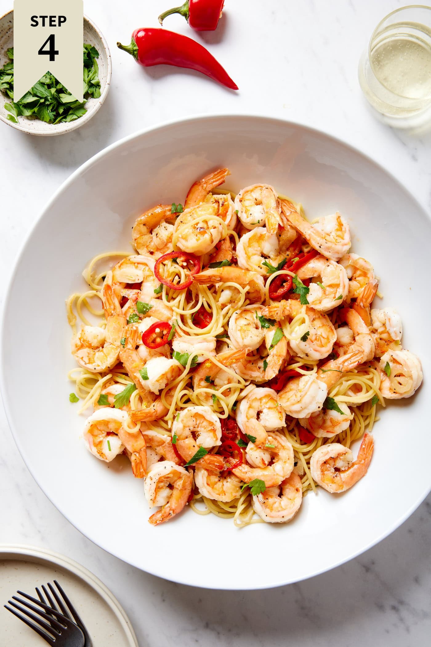 Large white bowl filled with garlic shrimp pasta with glass of white wine to the side.