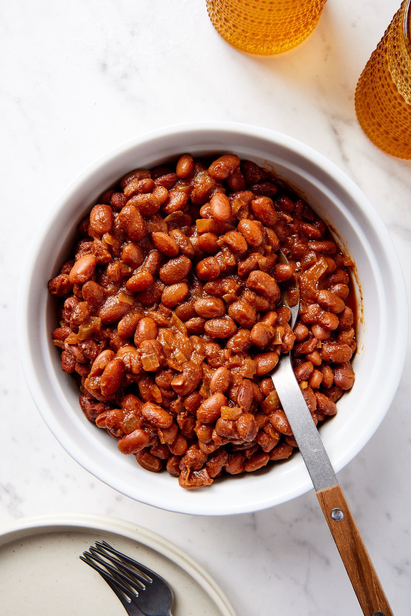 White round baking dish filled with bbq baked beans with spoon resting in dish all on white marble surface.