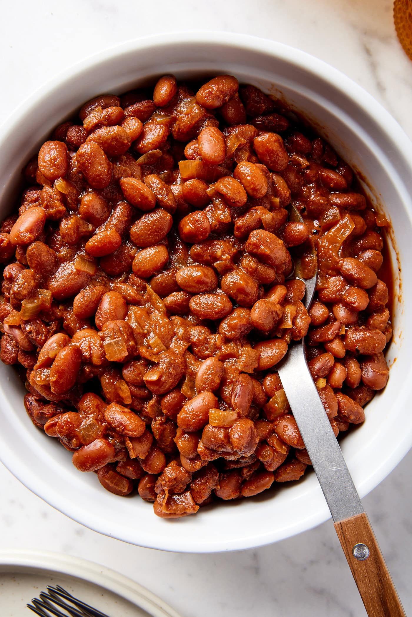 White round baking dish filled with cooked bbq baked beans with brown sauce all over the beans.