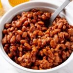 White serving dish filled with bbq baked beans with spoon resting in container ready for serving.