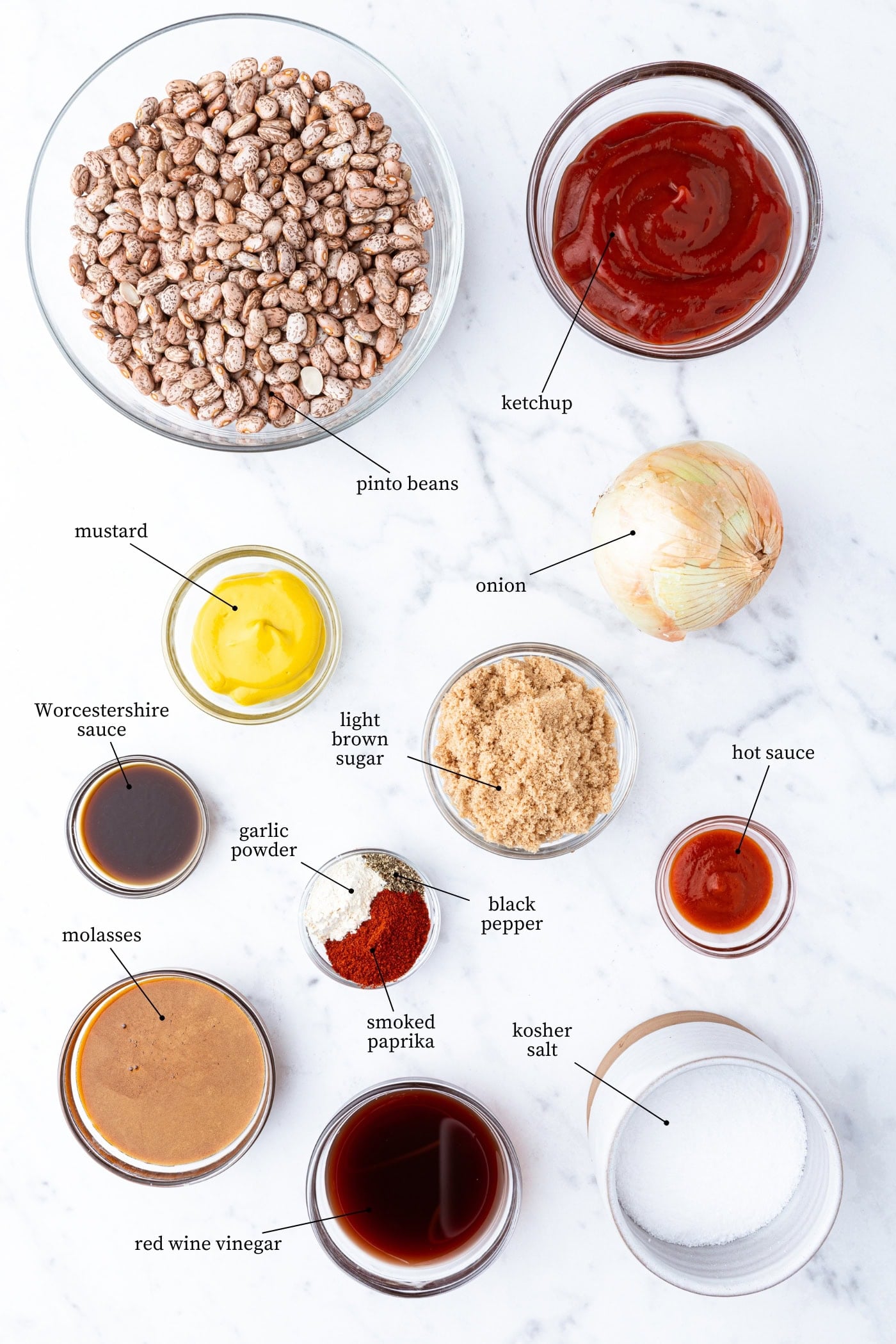 White marble surface filled with ingredients to make bbq baked beans including ketchup, mustard, beans, spices, and more.