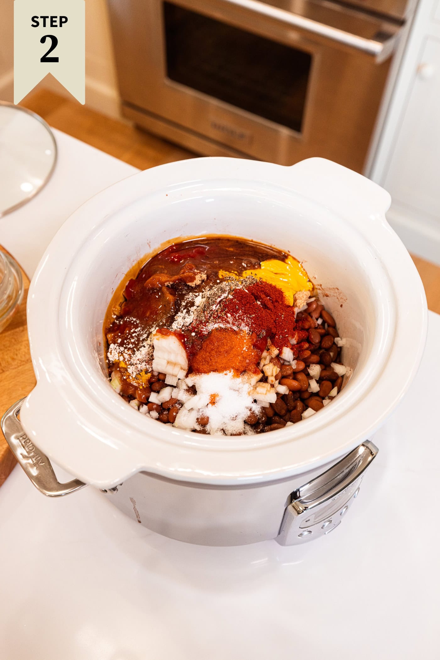 Slow cooker with dried and cooked beans with condiments on top to make a homemade bbq baked beans recipe.
