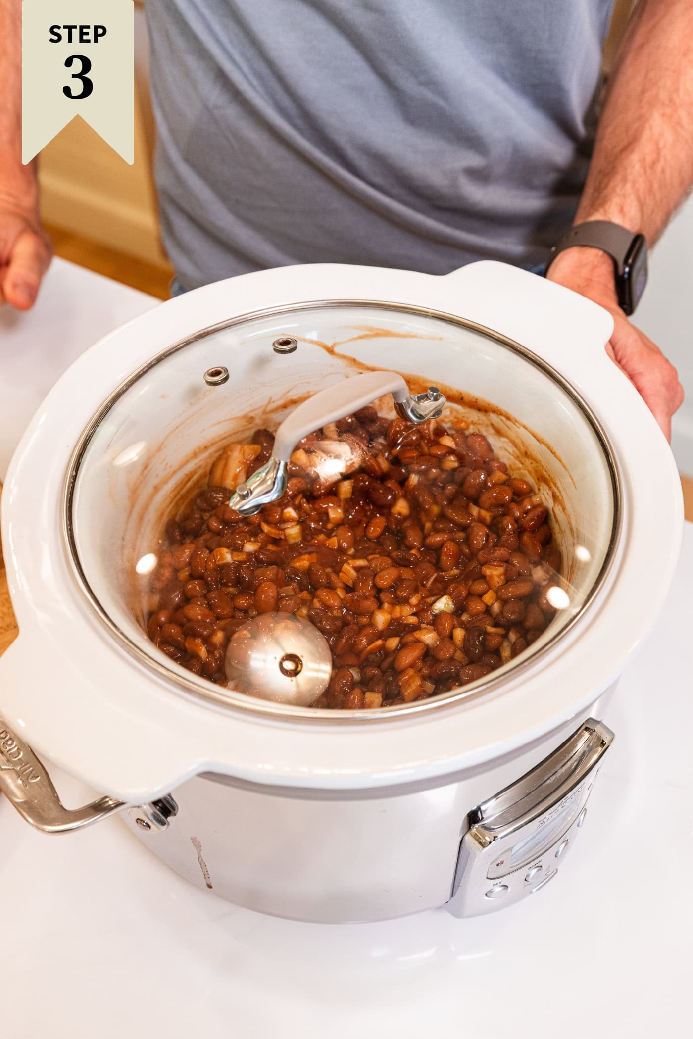 Lid sitting on a slow cooker with cooked bbq baked beans ready to be served.