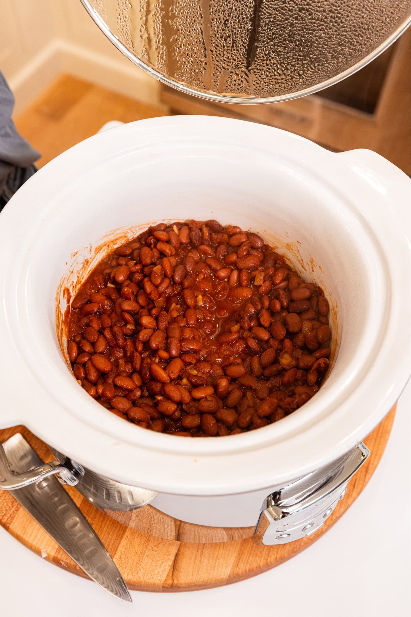 White slow cooker filled with cooked bbq baked beans after cooking for hours.