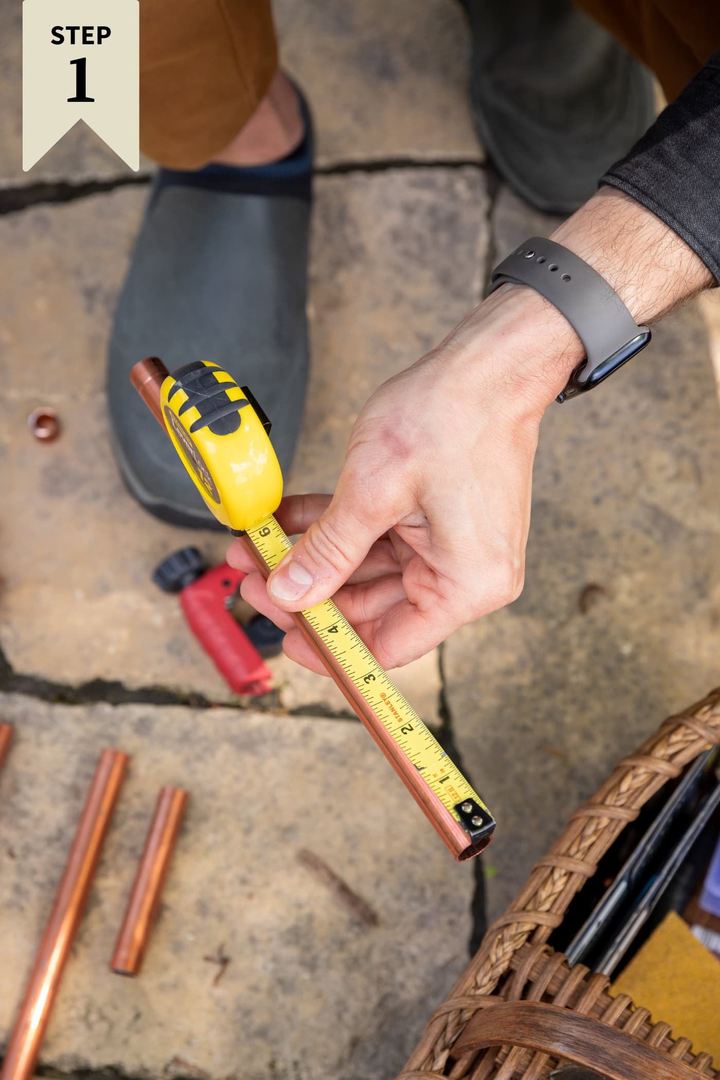 Measuring tape being drawn across a copper pipe for a certain measurement to be taken for DIY water fountain.
