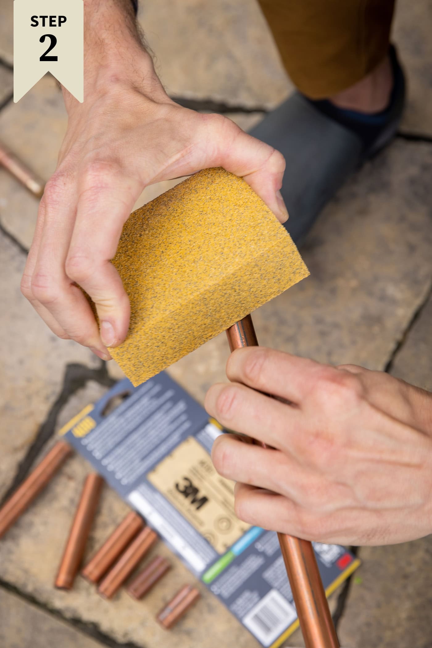 Piece of sandpaper roughing up the edge of a copper pipe before being fitted together for a DIY water fountain.