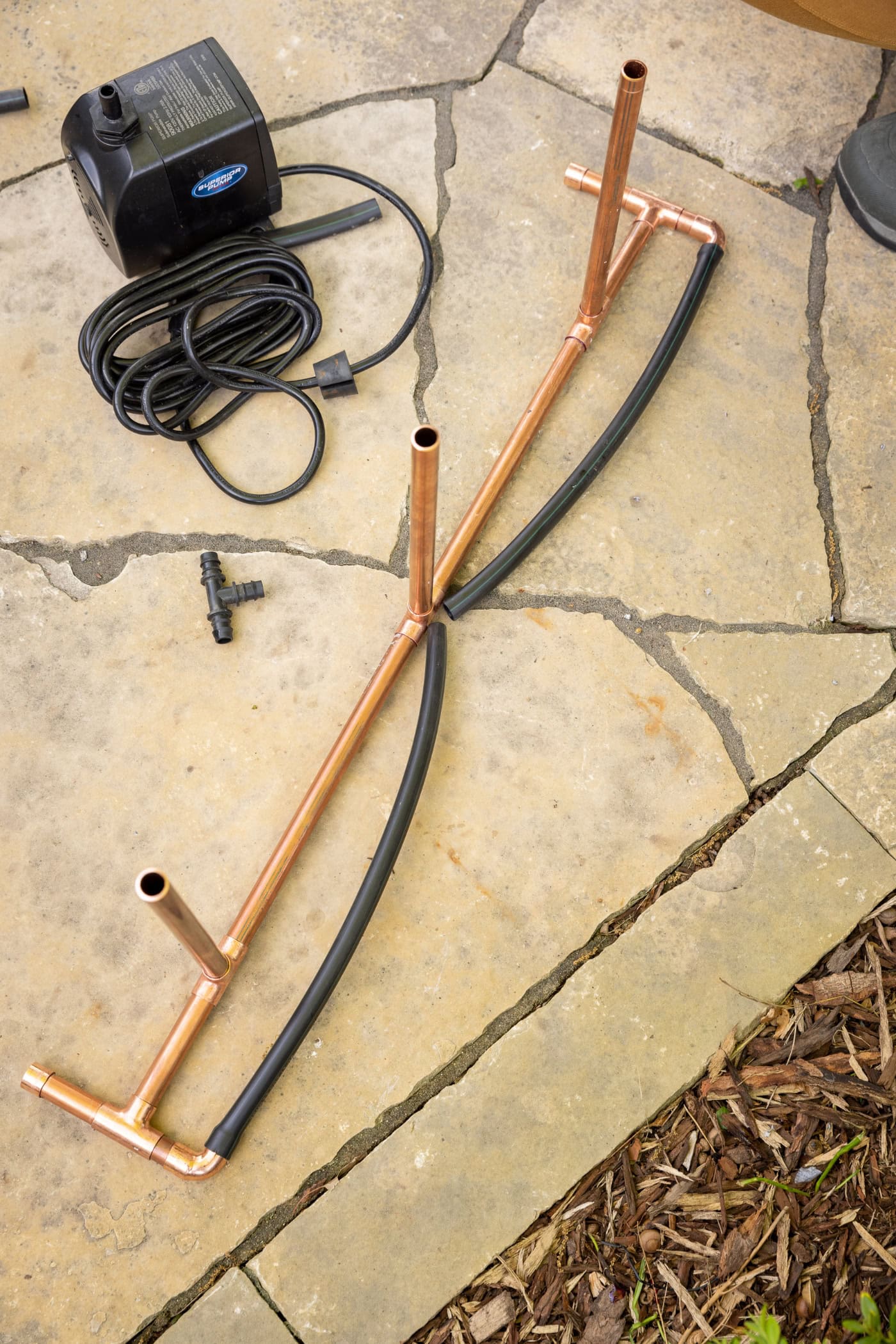 DIY water fountain made from copper pipe with a black rubber hose completing the circuit.